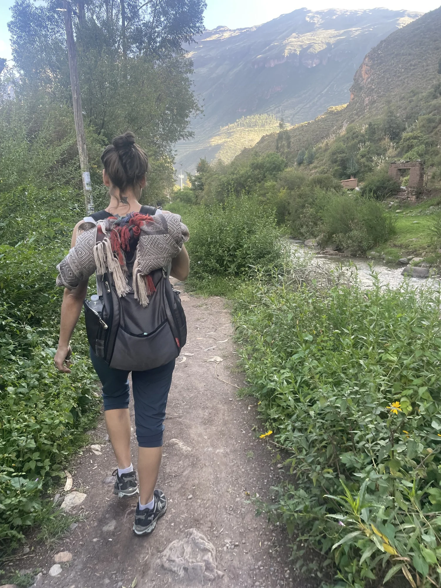 Hiker on a dirt trail beside a river with mountains in the background