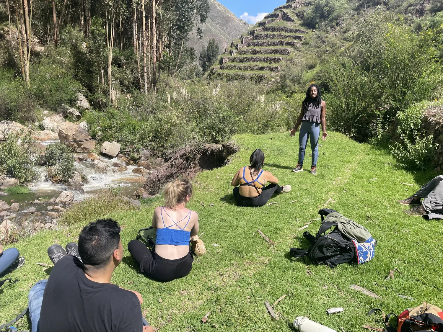 Group relaxing beside a creek surrounded by lush green hillside