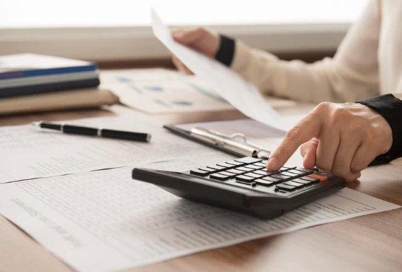 Person using a calculator and reviewing documents on a desk.