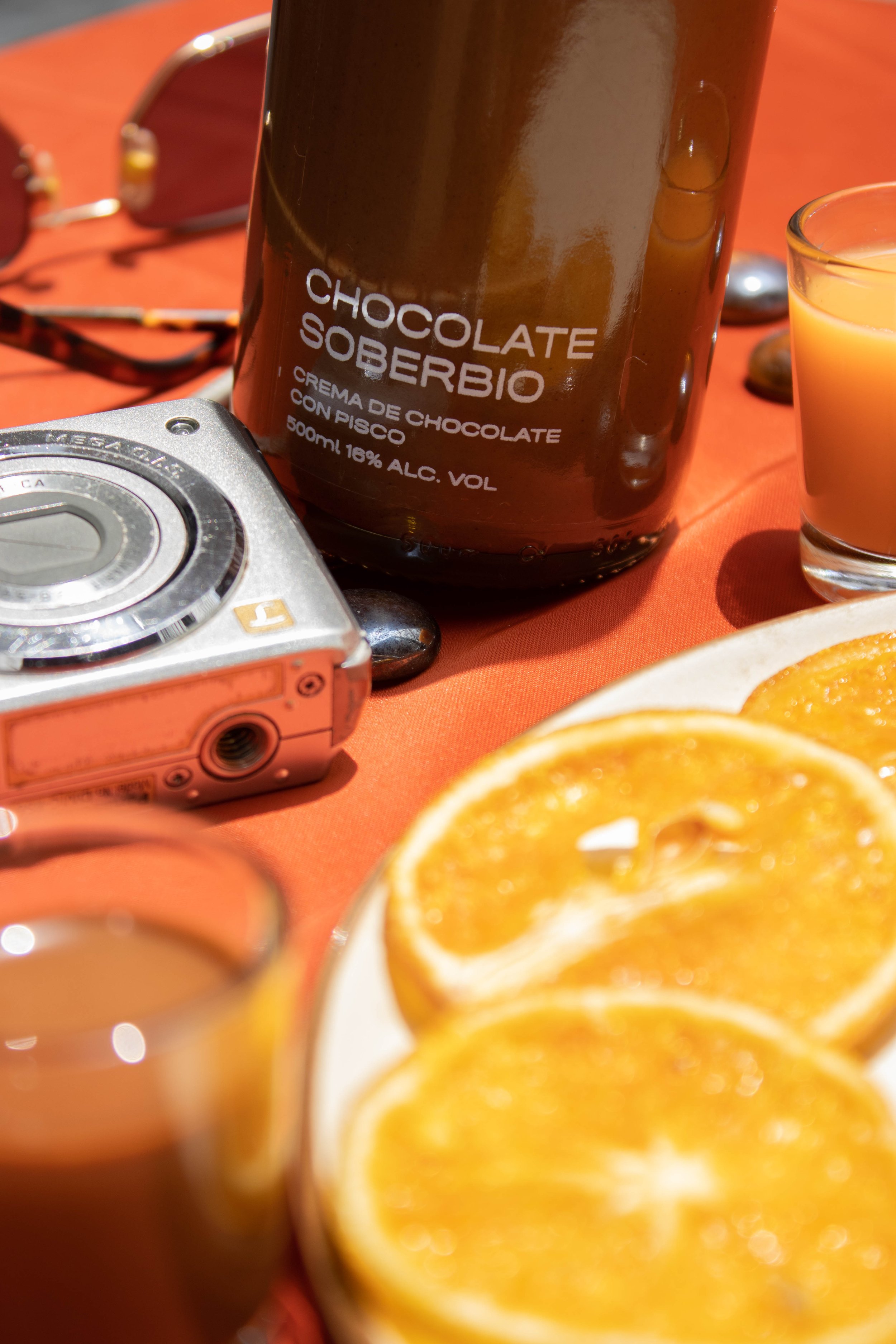 Botella Chocolate Soberbio de 7 Pecados junto a naranja fresca, crema de pisco peruana sabor chocolate ideal para sobremesa, cócteles y celebraciones premium.