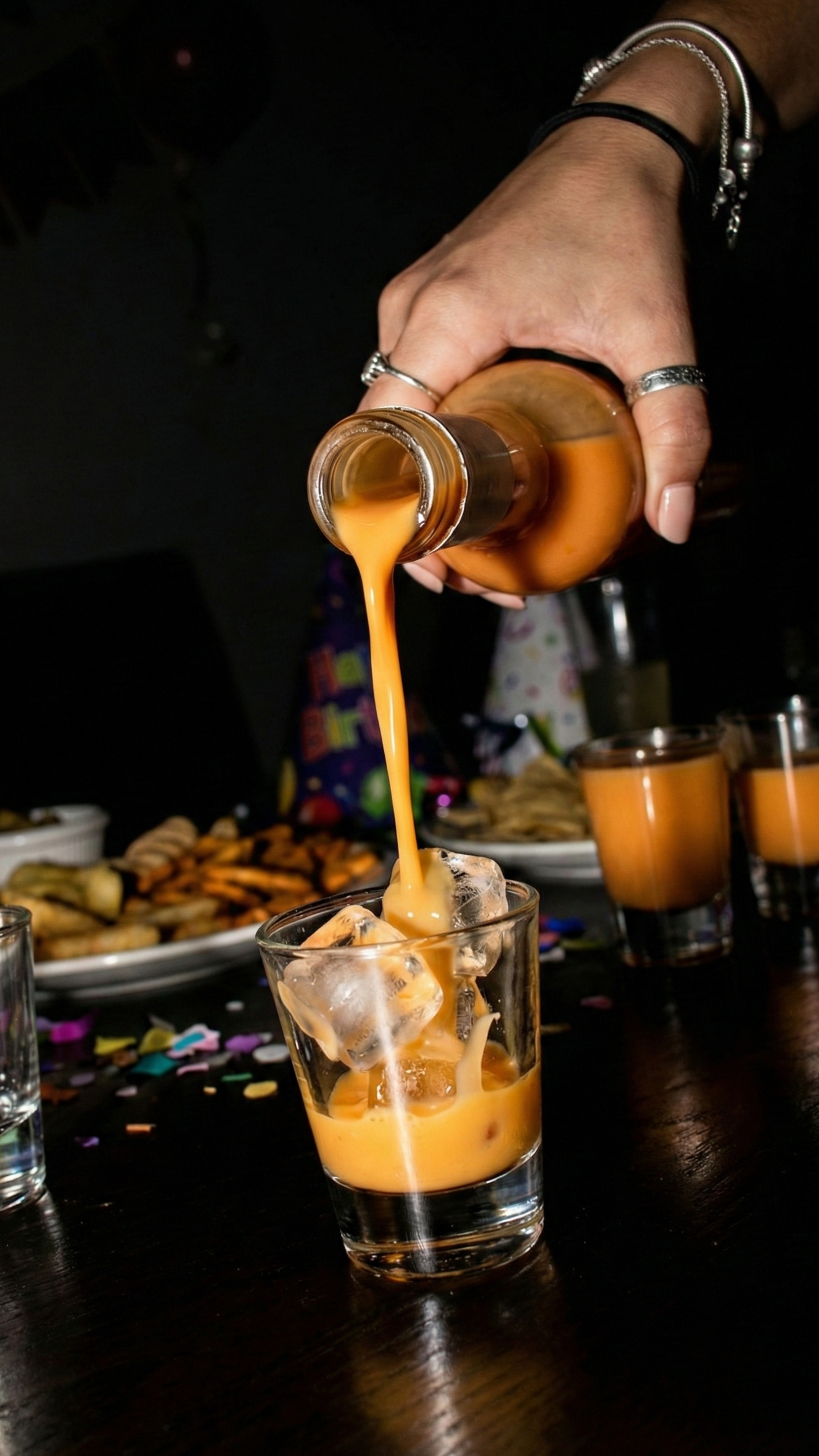 Sirviendo crema de pisco 7 Pecados Lúcuma Golosa sobre hielo en celebración nocturna, licor cremoso premium ideal para fiestas y reuniones en Lima.