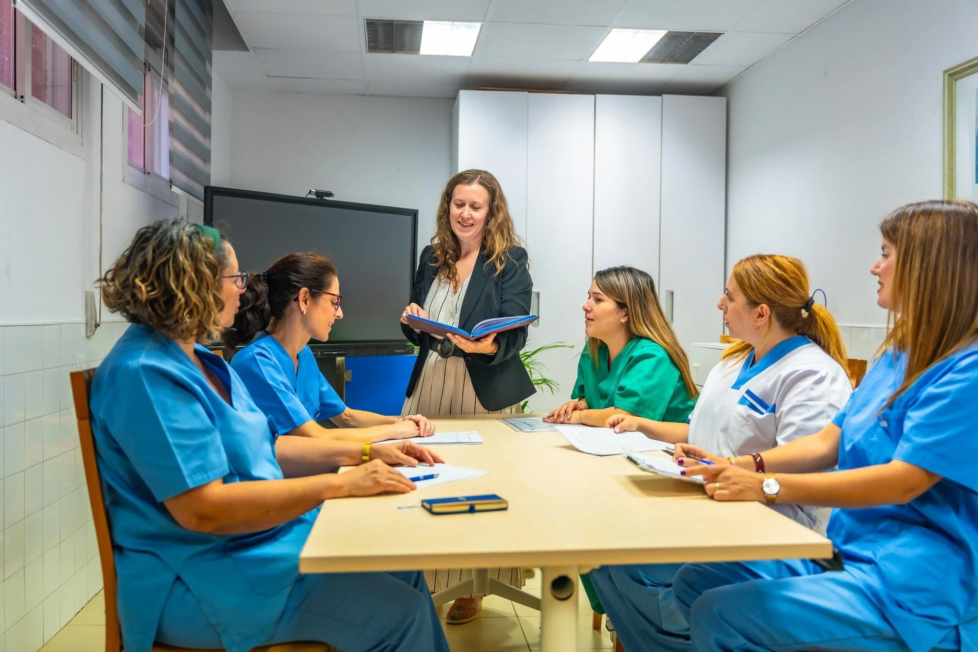 A group of female caregivers and a woman instructor in a business suit training caregivers around a conference table in Cognihealth home care office.