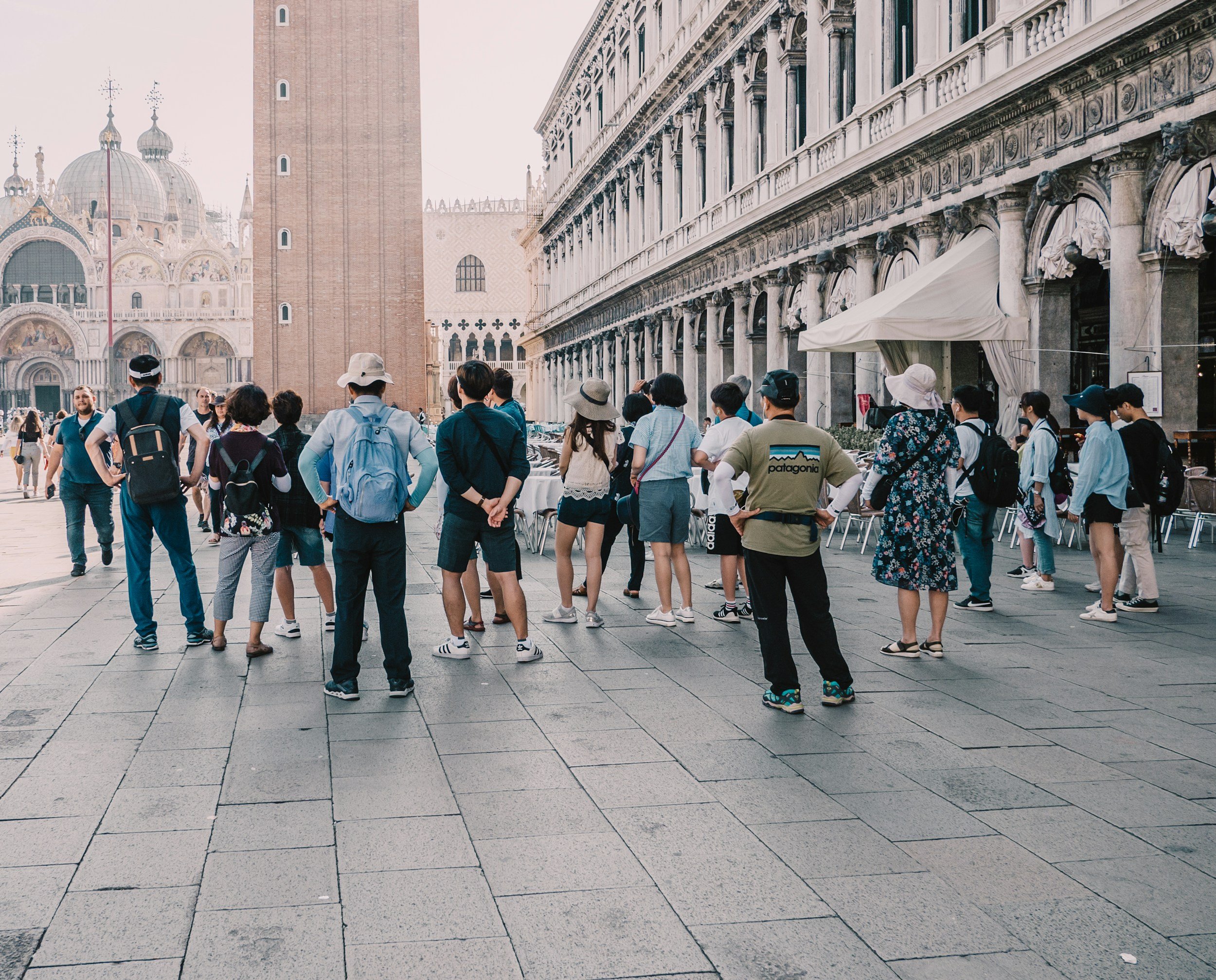 Group of tourists gathered outside a historic building in Venice, Italy, with domed architecture visible in the background.