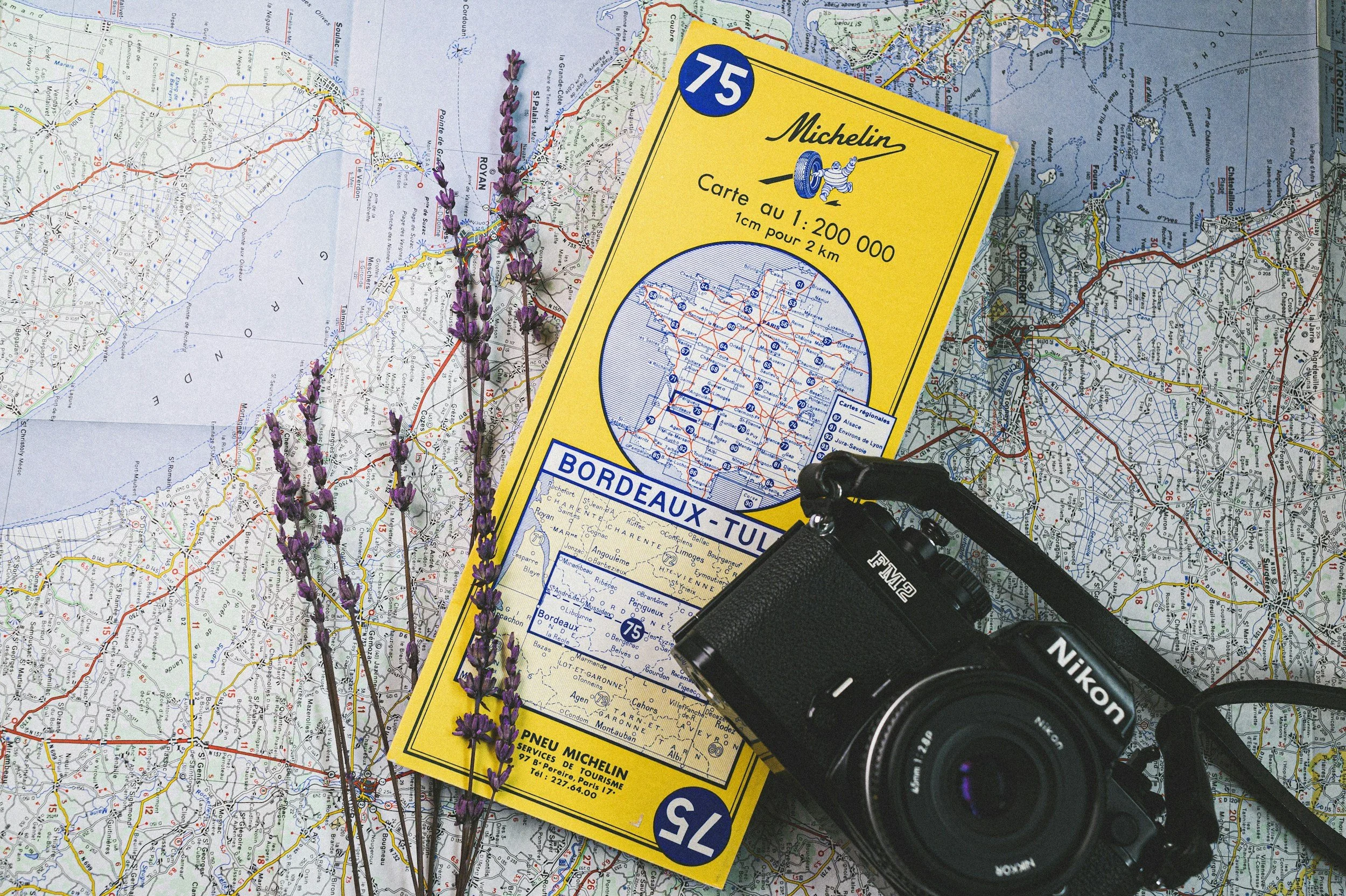 A map of rural France with a yellow Michelin map scale guide, some lavender flowers, and a black Nikon camera on top.