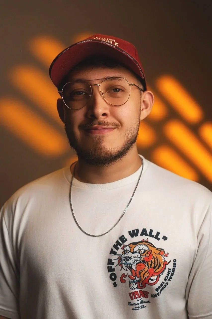 Joven con barba, gafas de oro, gorra roja y camiseta blanca con logotipo de un tigre y letras 'OFF THE WALL'
