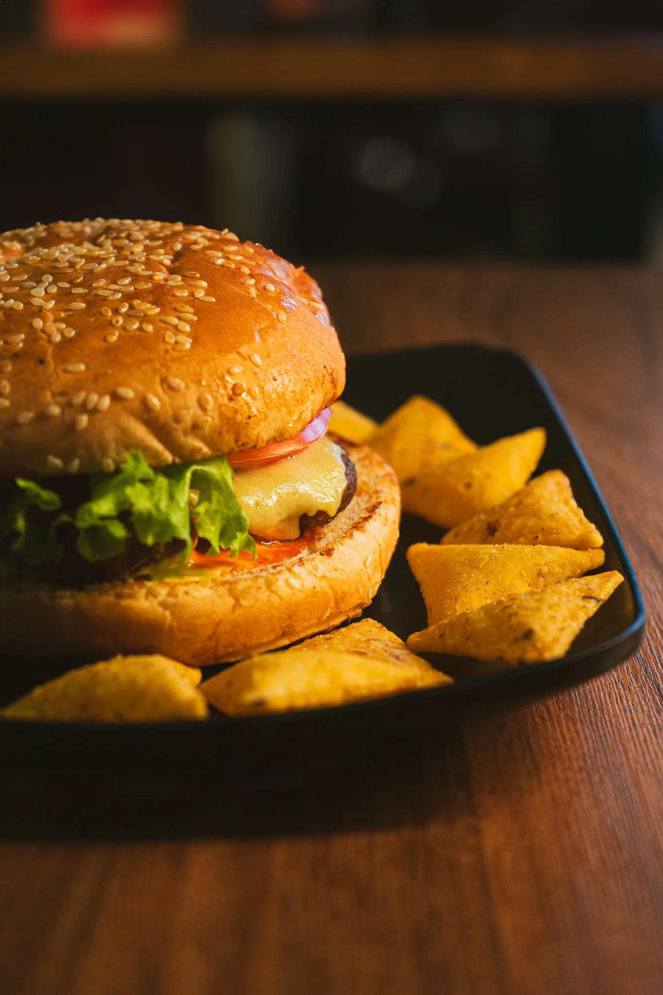 Hamburguesa con papas fritas en plato negro sobre mesa de madera.