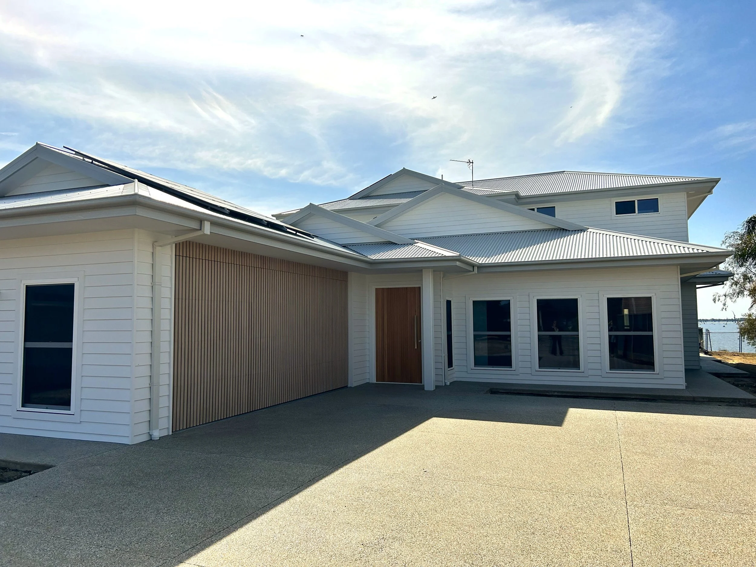 A modern two-story house in Yarrawonga Victoria clad in weatherboard with a Colorbond roof, featuring double hung windows and a custom-made timber look aluminum slat entrance door and double garage door, situated on Lake Mulwala.