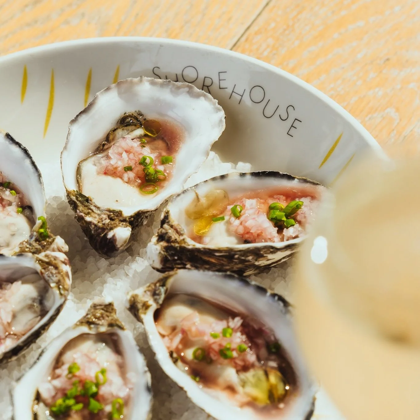 Close-up of oysters on a plate, garnished with chopped green onions, served on a bed of ice at a restaurant named 'SCOREHOUSE'.