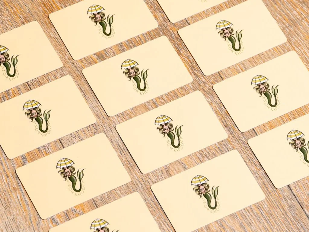 Several blank cards with a logo featuring a jellyfish wearing sunglasses and holding a yellow checkered umbrella, laid out on a wooden surface.