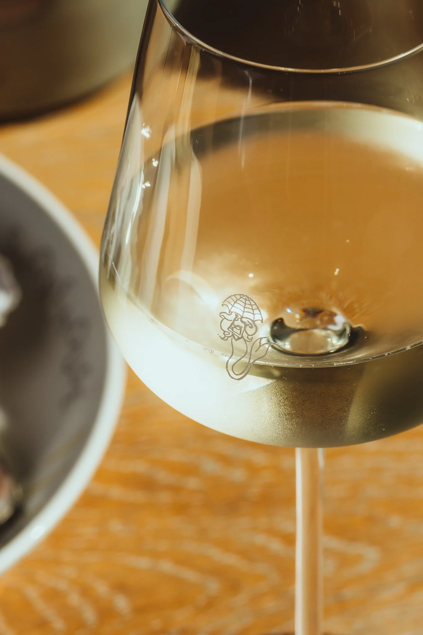 Close-up of a glass of dark beverage, possibly wine or red juice, on a wooden surface, with part of a second glass and a white straw visible.