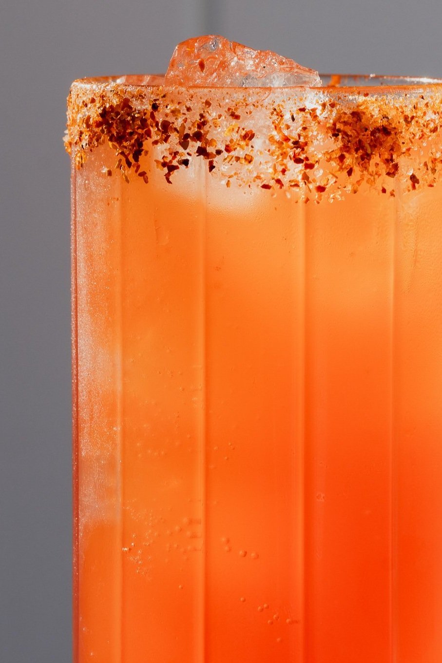 A close-up of an orange cocktail in a tall glass with a salted rim, ice cubes on top, and tiny bubbles in the liquid.