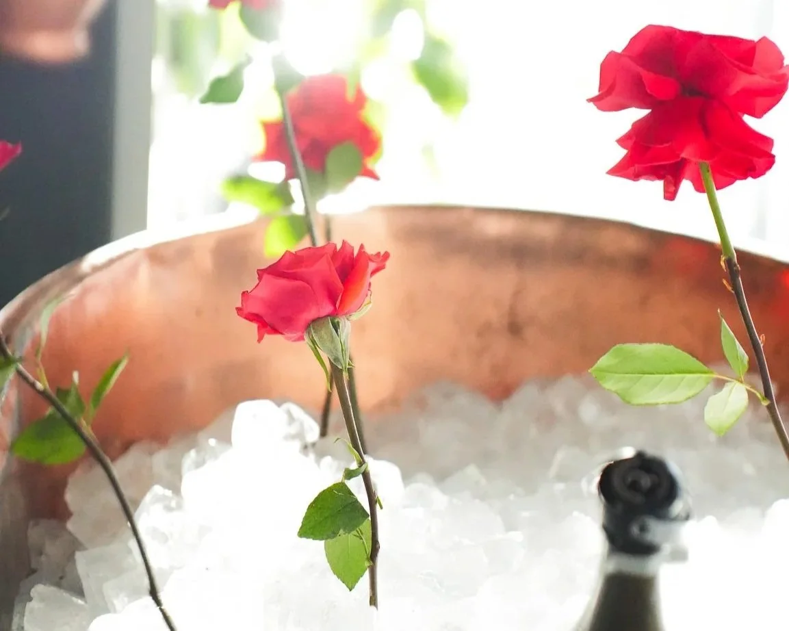Red roses in a copper bowl filled with ice, with a bottle of champagne nearby.