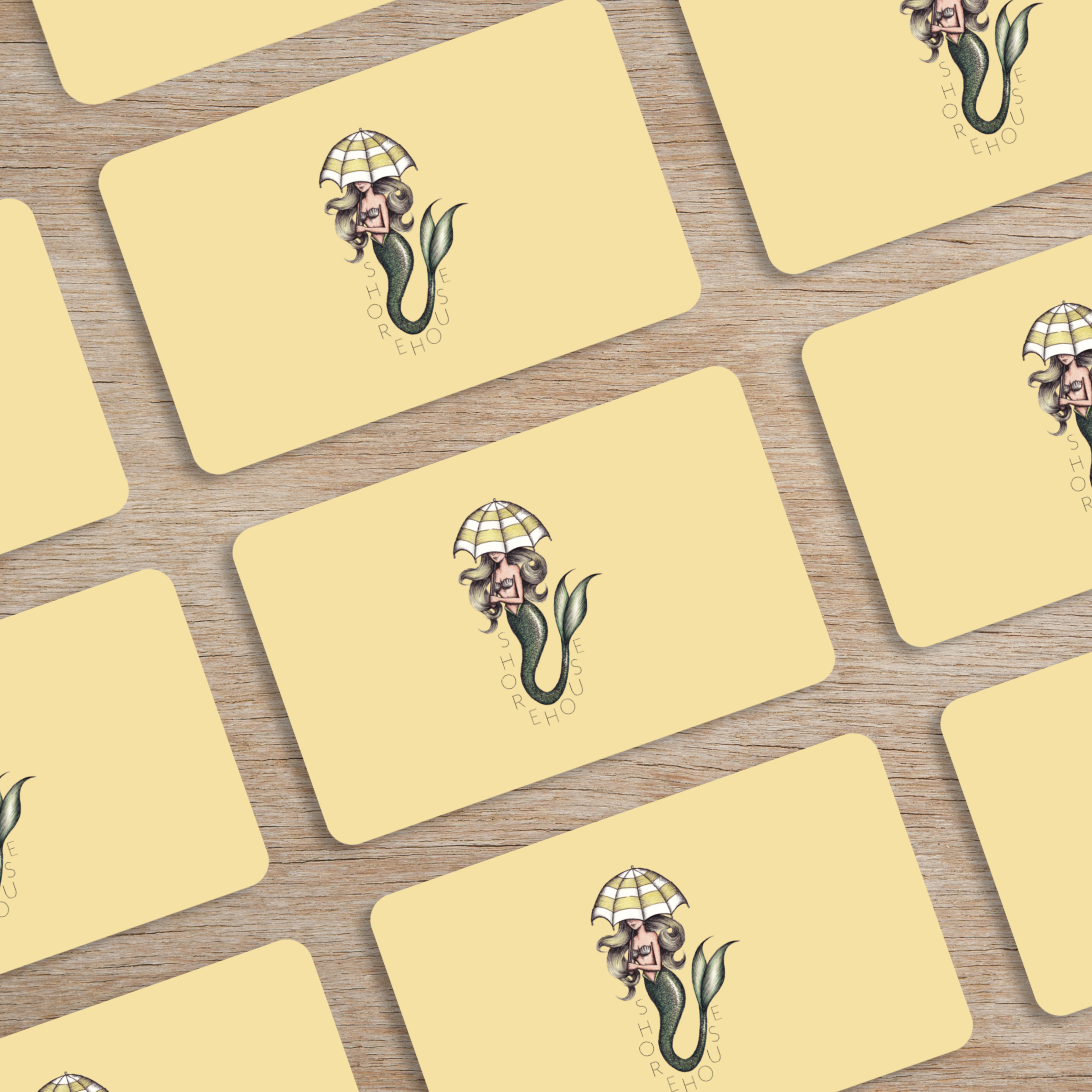 Multiple yellow cards with a mermaid holding an umbrella and the words 'SHOREHOUSE' on a wooden surface.