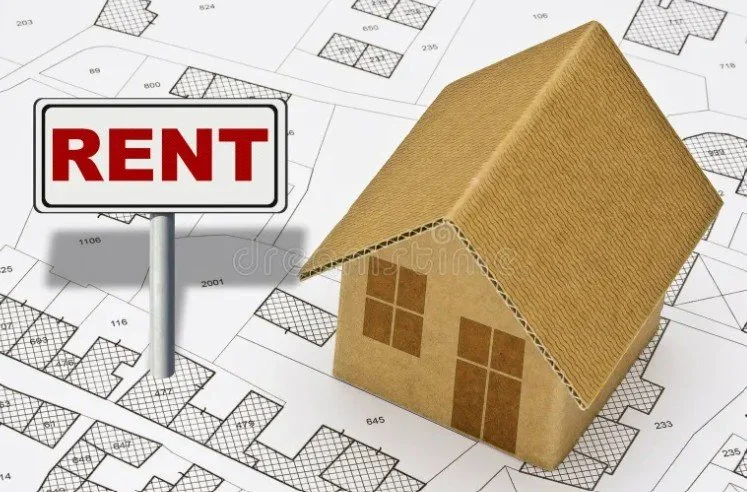 Cardboard model house with a tiled roof on an architectural blueprint, next to a sign that says 'RENT'