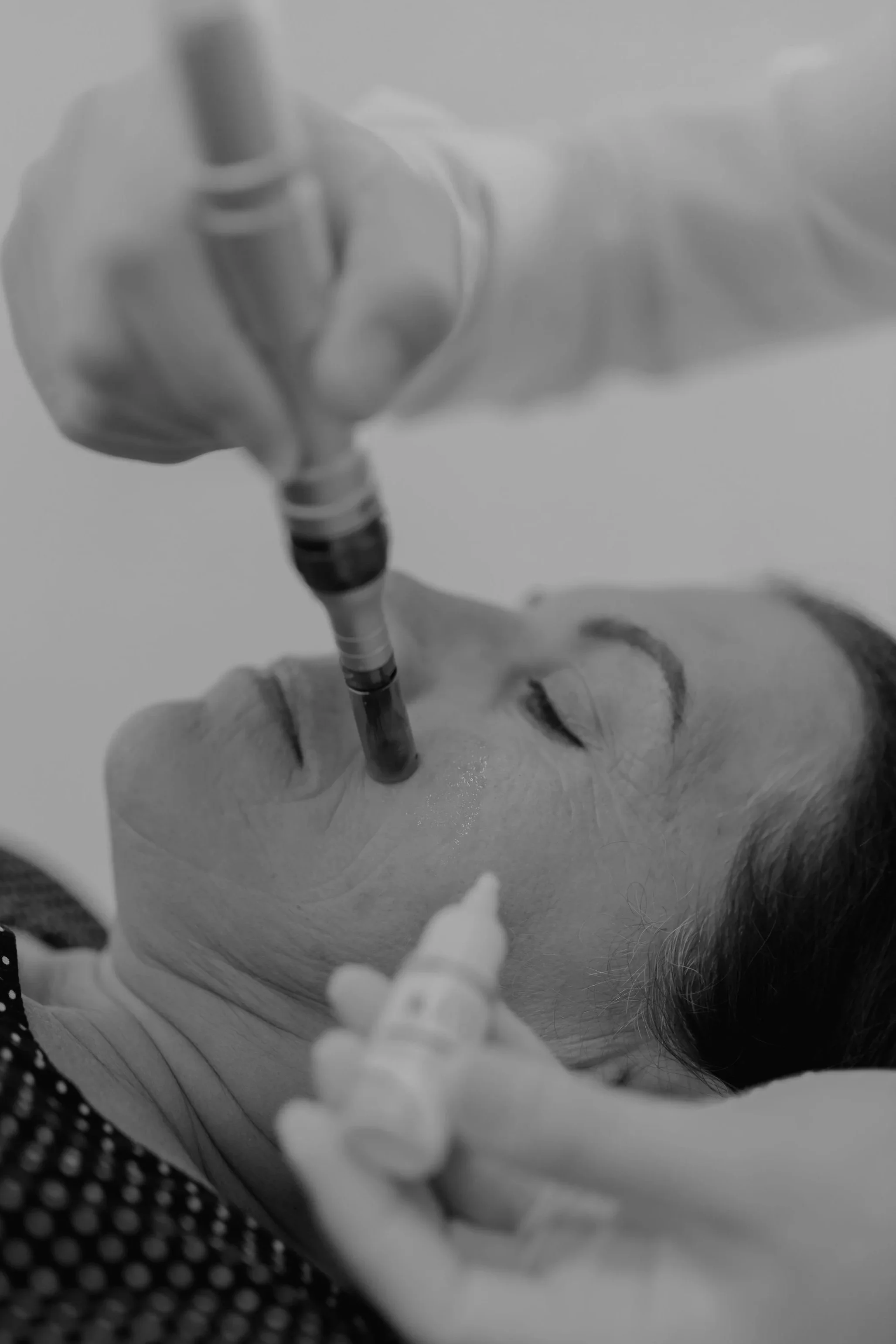 A person with a tattoo on their chest is lying down, holding a large syringe close to their chest. The photo is in black and white.