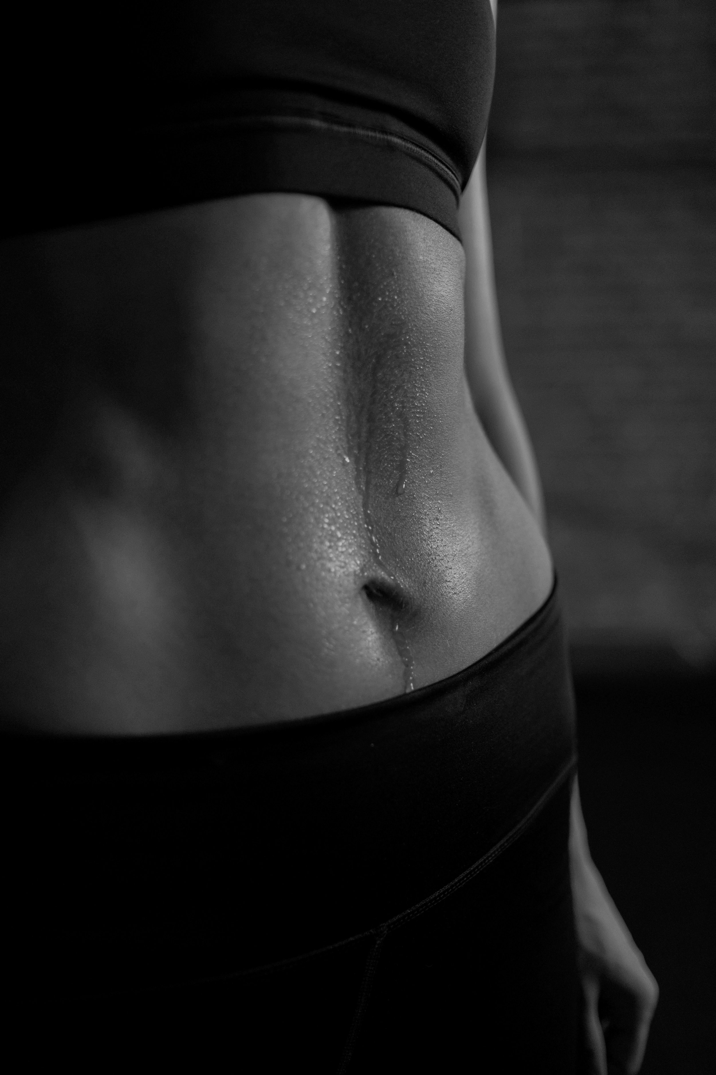 Close-up of a person's midsection showing the skin, belly button, and part of athletic clothing, with water droplets on the skin.