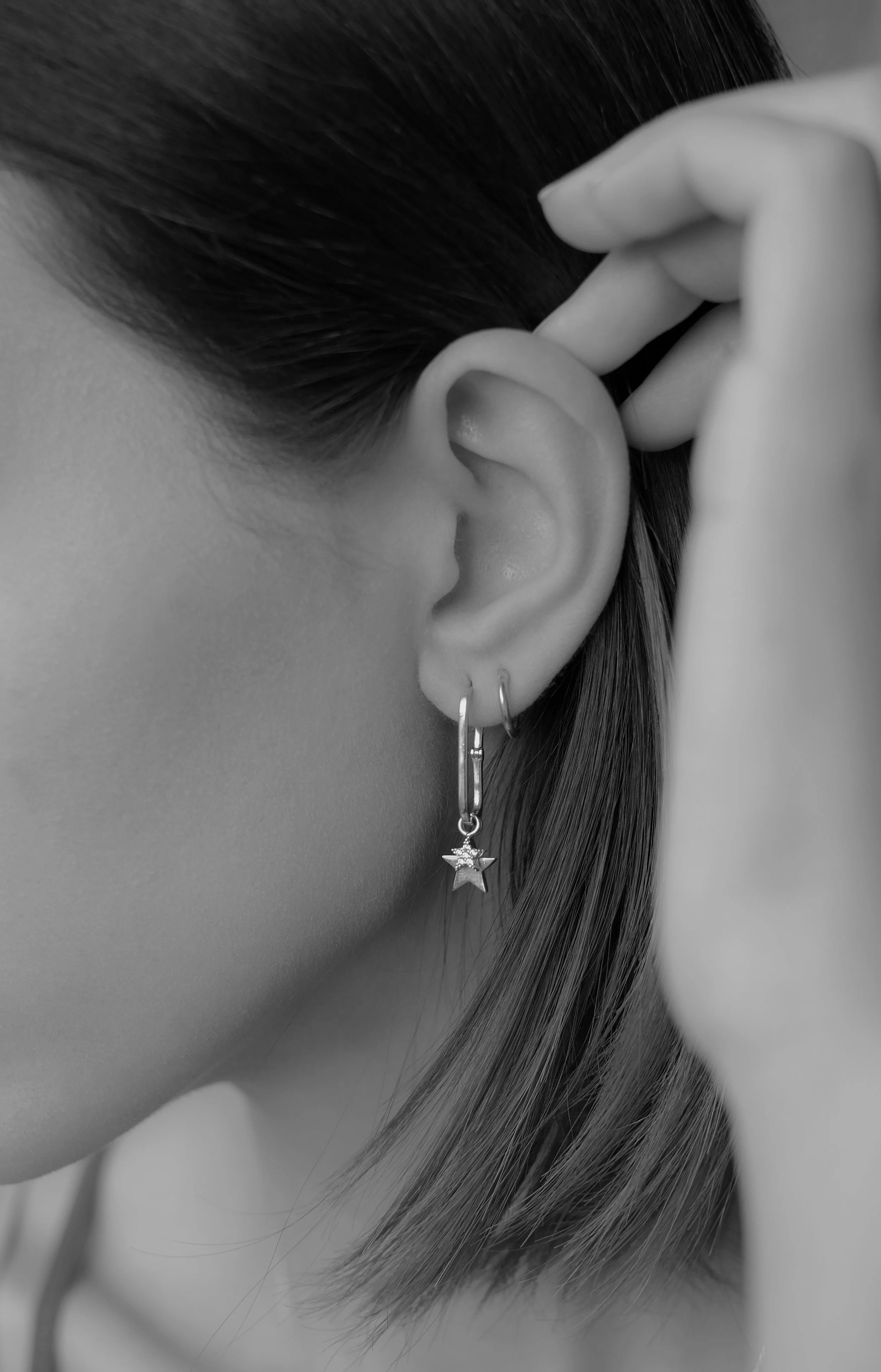 Close-up of a person's ear with a hoop earring featuring a star charm, touching their hair with fingers.