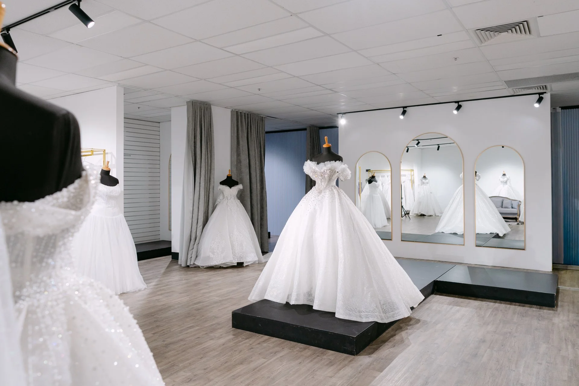 Store display of white wedding dresses on mannequins and a clothing rack, with large mirrors on the wall reflecting the dresses.