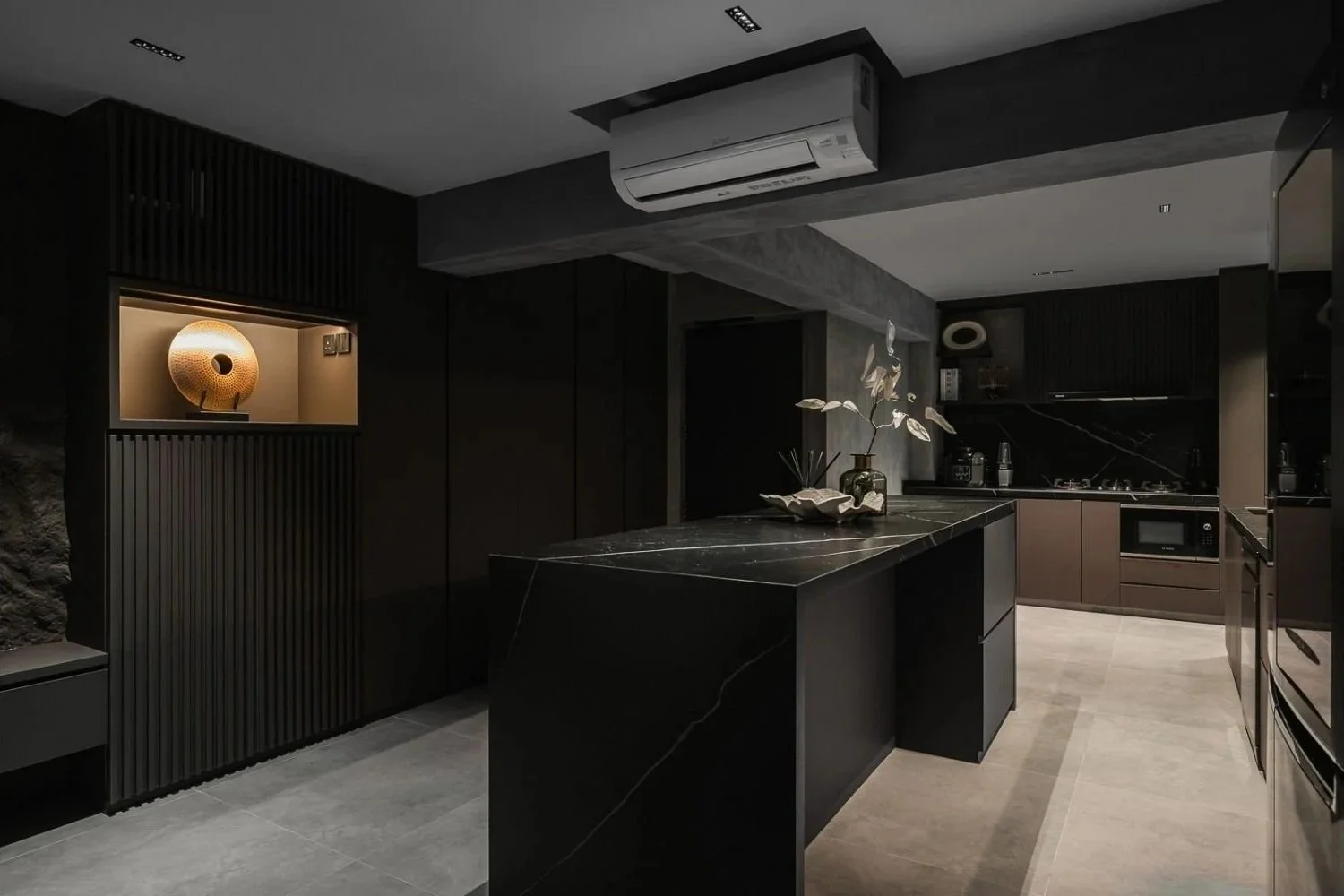 Modern dark kitchen with black countertops, cabinetry, and a black island, accented by decorative objects and a small vase with white flowers.