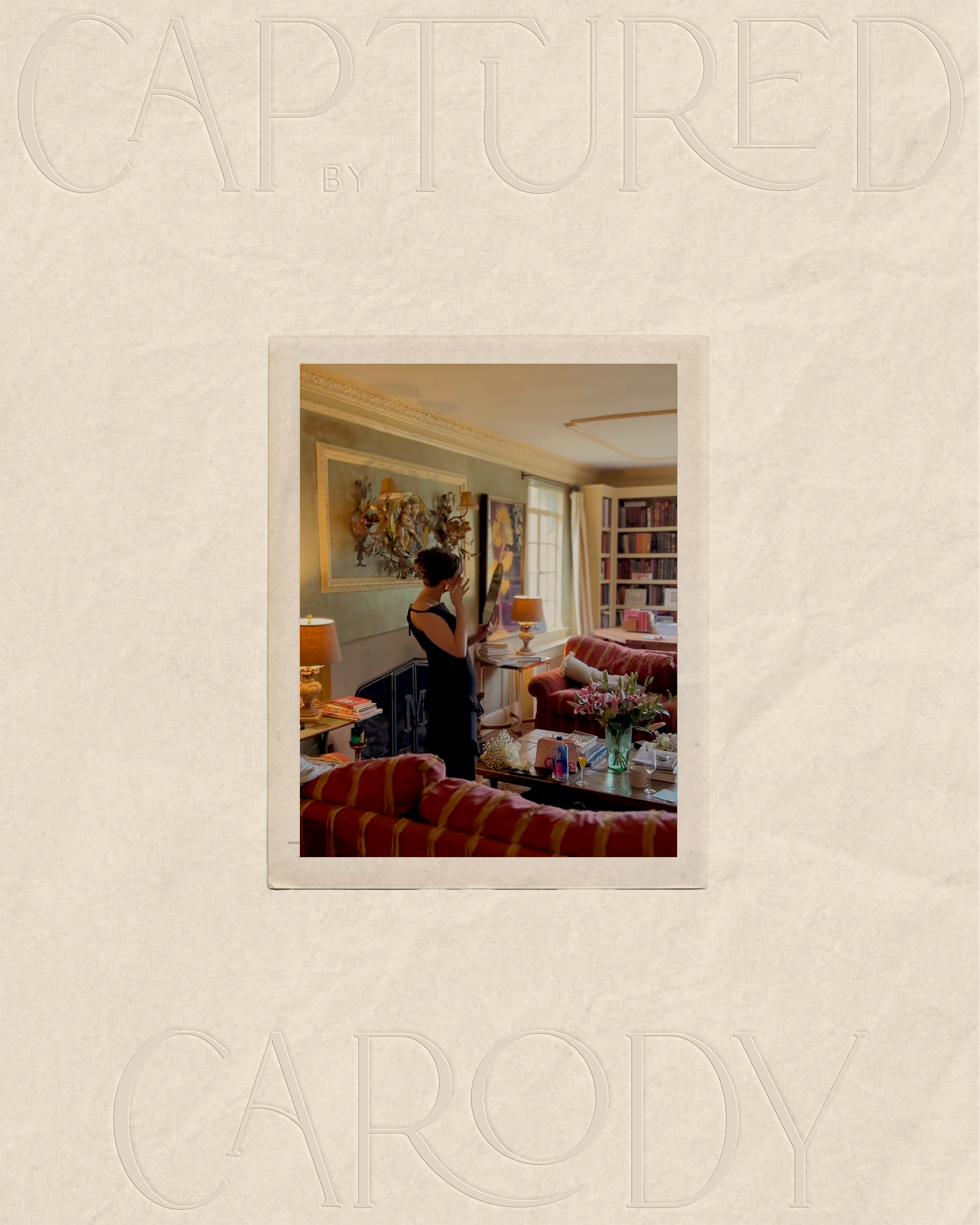 A woman in a black dress is standing in a living room, holding a tissue or napkin near her face. The room has a sofa with red and gold striped fabric, a coffee table with flowers and drinks, and a wall with artwork. There are several lamps, a bookshe