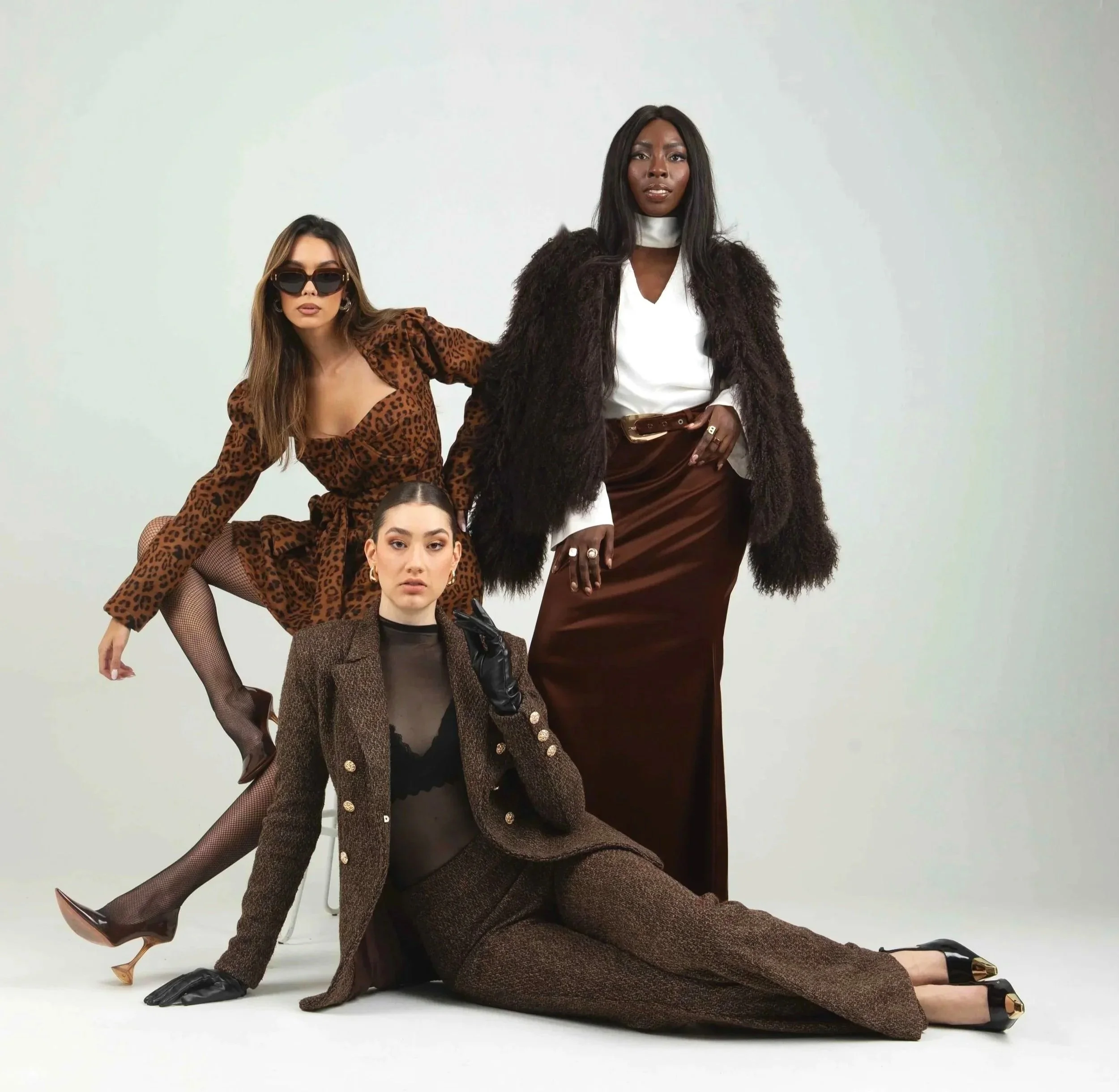Three women dressed in stylish, coordinated fashion with animal prints and brown tones posing in front of a plain background.