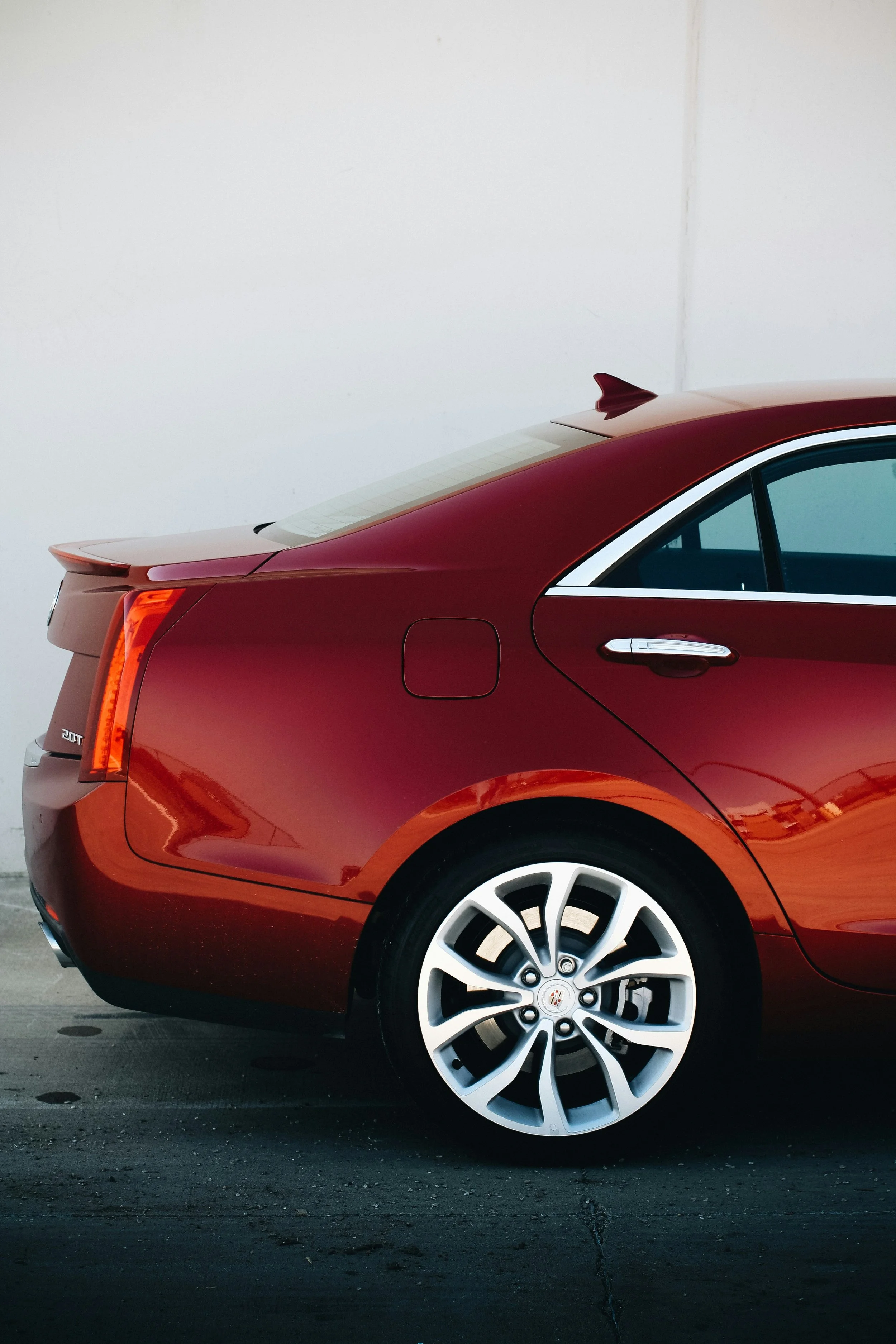 Red Cadillac sedan parked against a plain white wall, showing the rear and side.