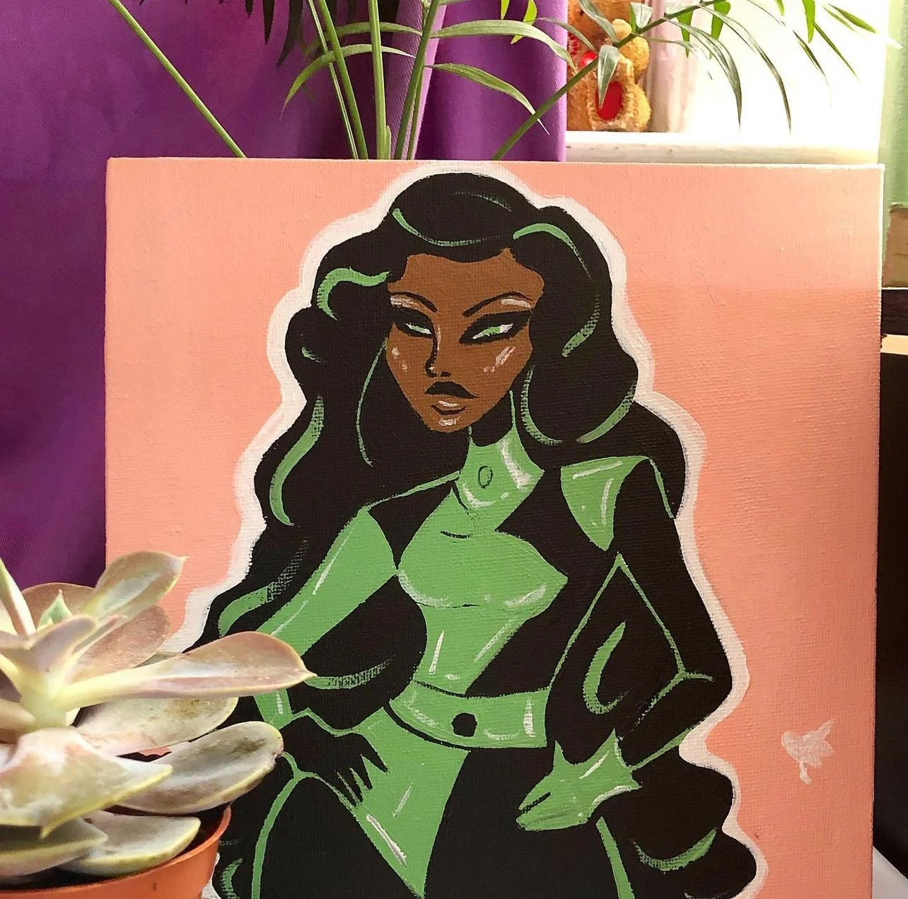 A colorful illustration of a woman with long, black hair with green streaks, wearing a green and black outfit, depicted on a pink background. There are plants and a purple wall visible around the artwork.