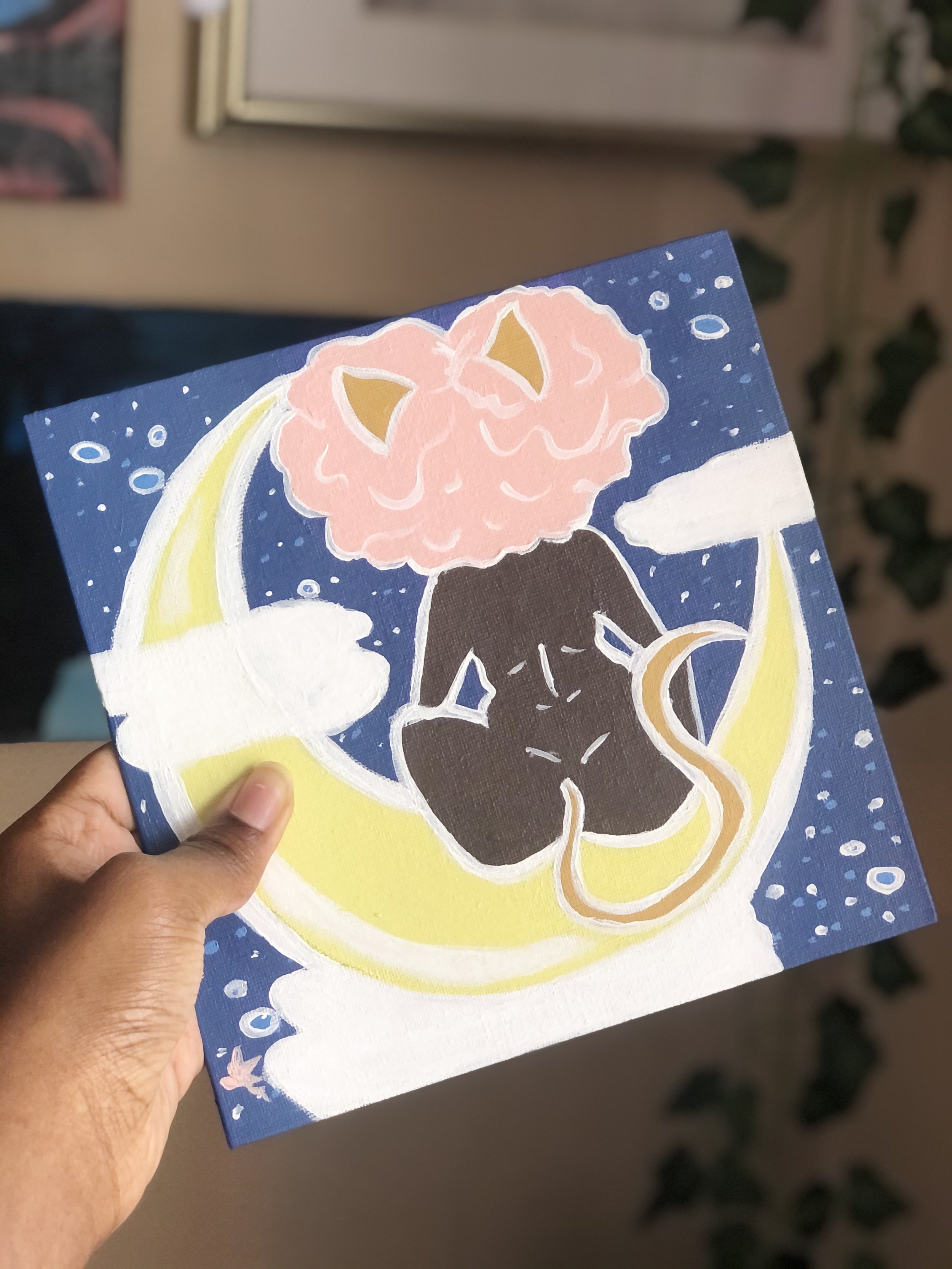 An illustration of a black cat with a pink fluffy head resting on a crescent moon against a night sky with stars and clouds.