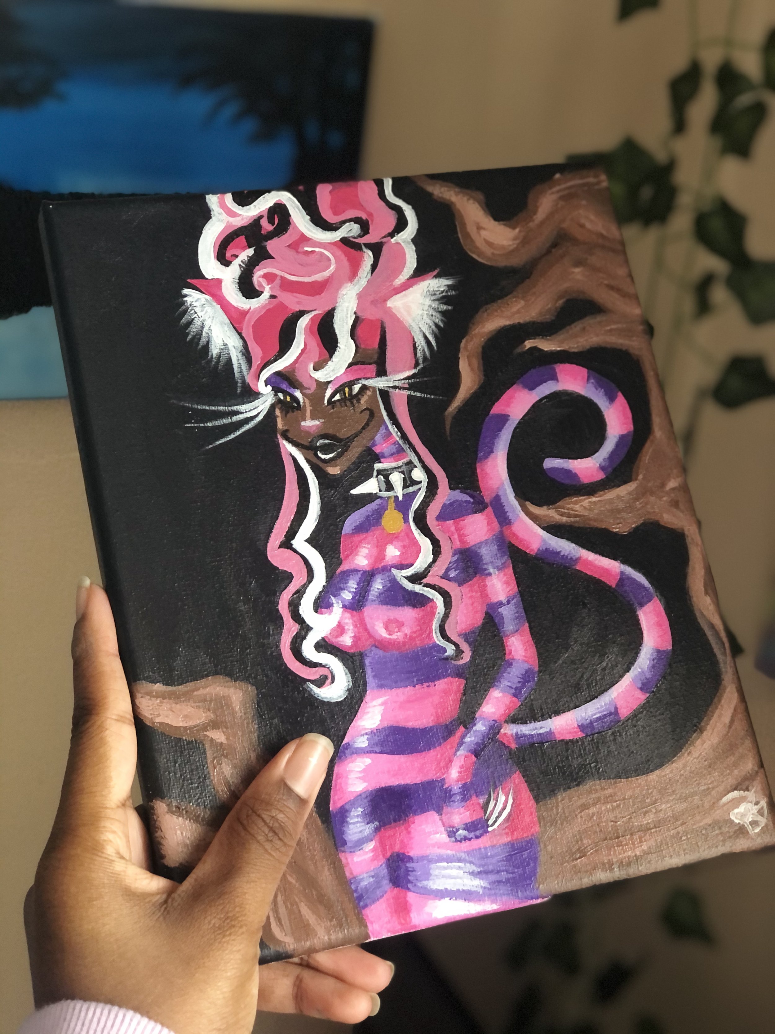Hand holding a colorful painting of a fantasy cat character with striped tail and hair, set against a dark background.
