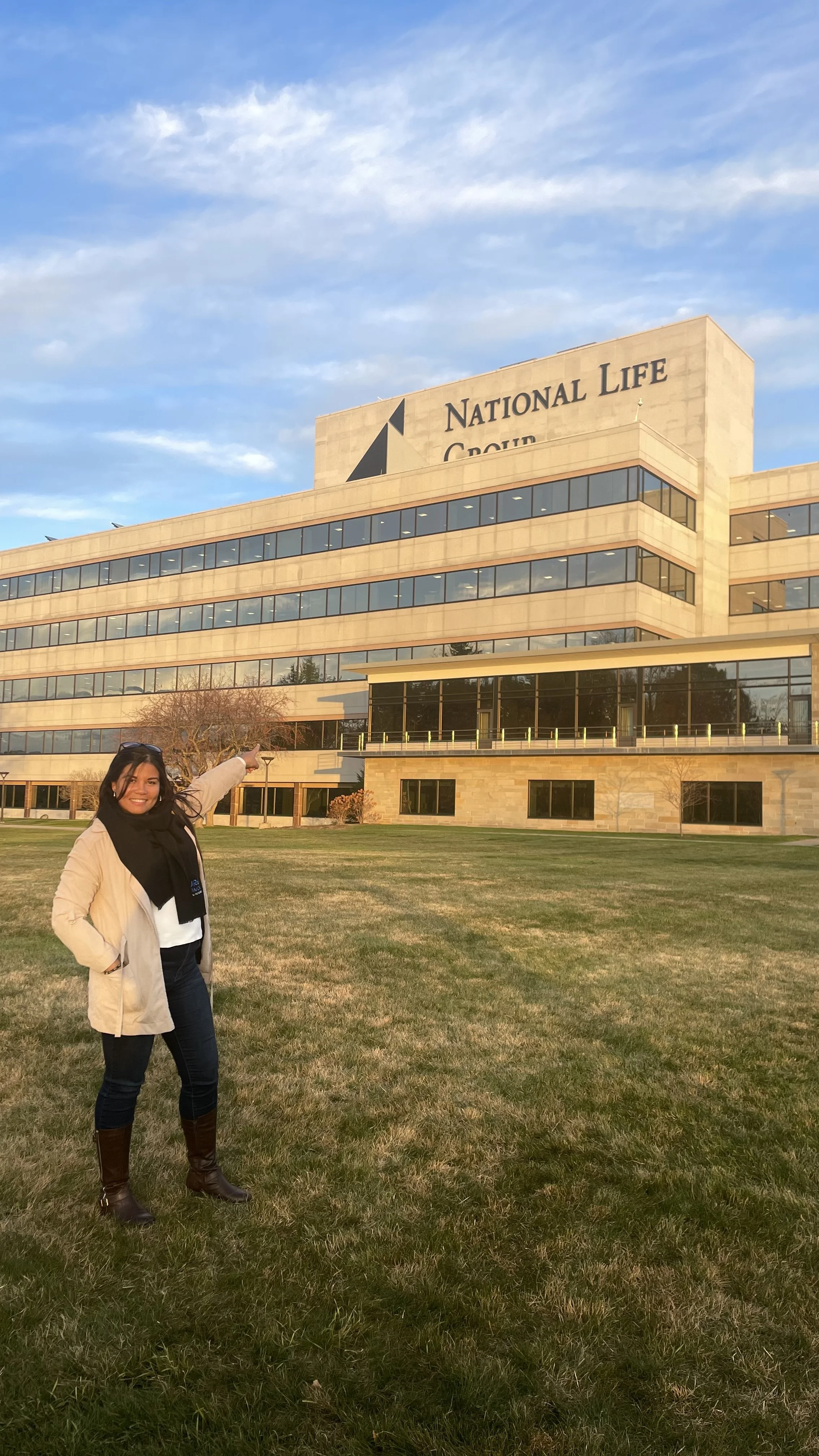 Mujer sonriendo y señalando el edificio de la sede de National Life Group en un día soleado.