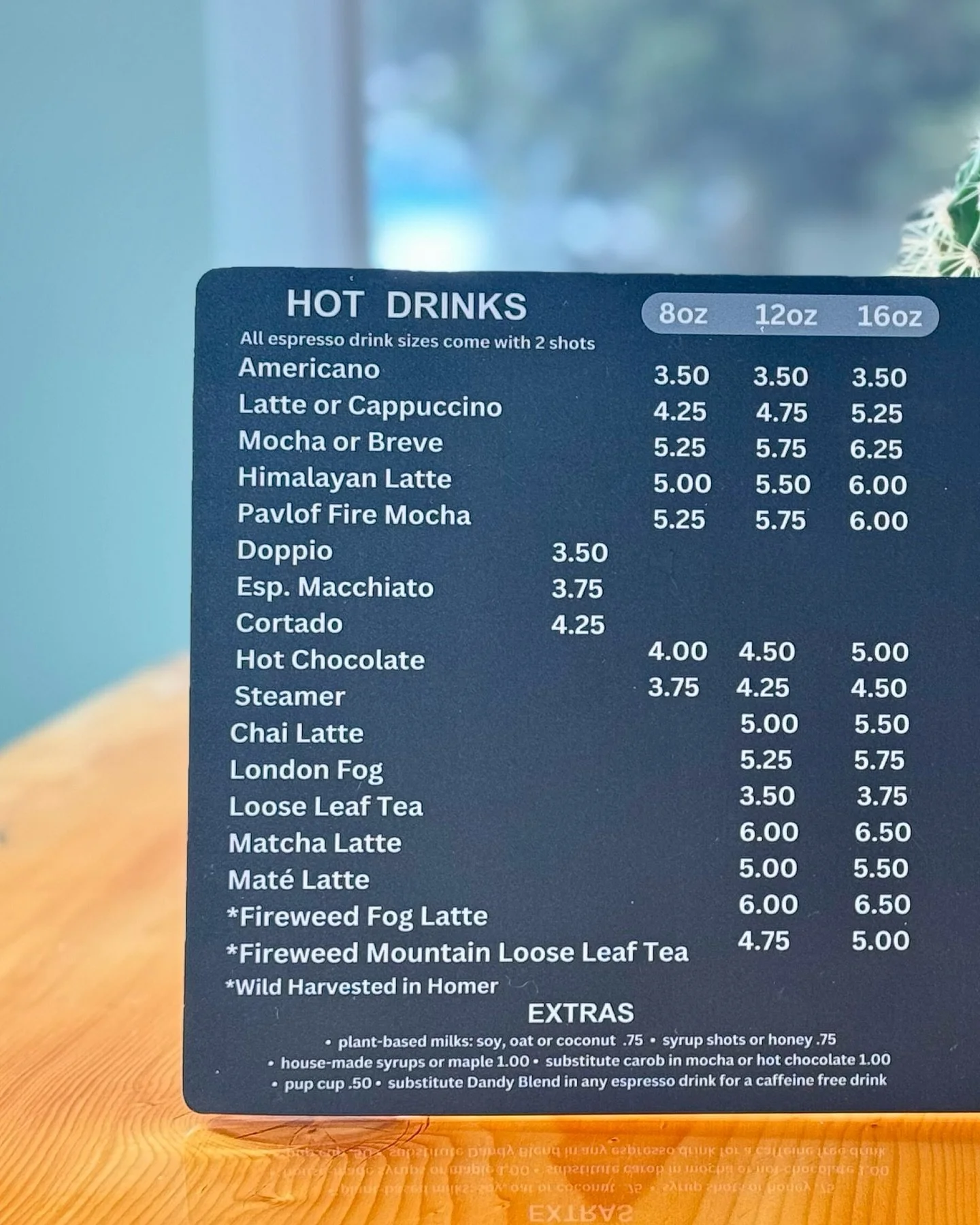 A menu of hot drinks with prices listed for different sizes, including espresso, lattes, mochas, teas, and specialty drinks on a blue background.