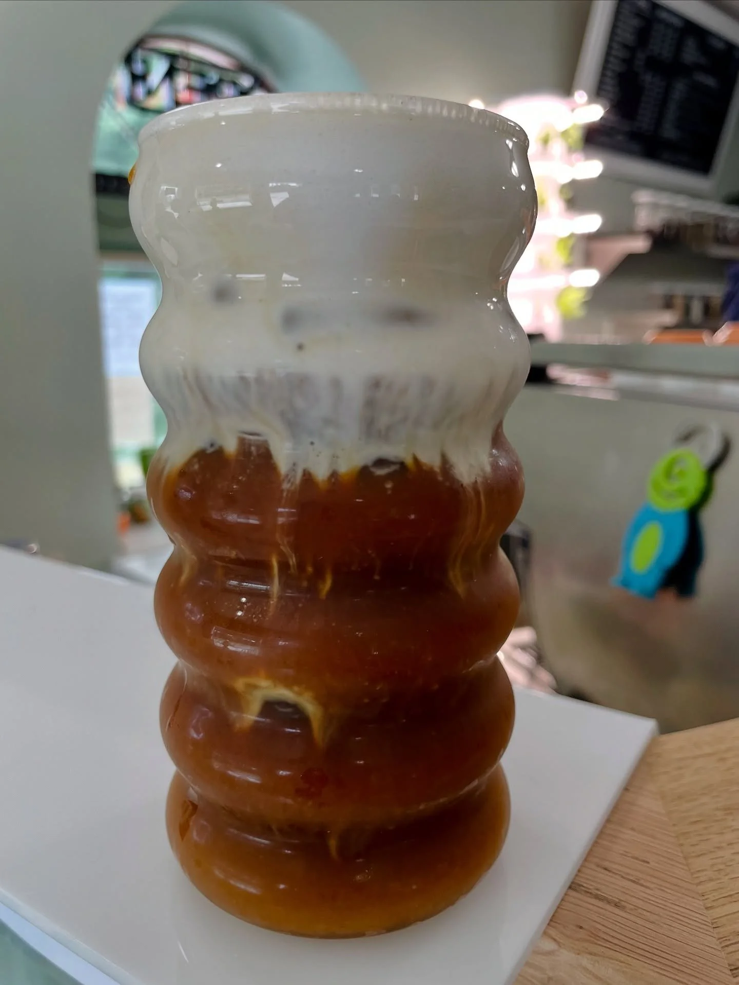A tall, wavy glass vase with a gradient from white lavendar cold foam at the top to amber at the bottom, placed on a white surface.