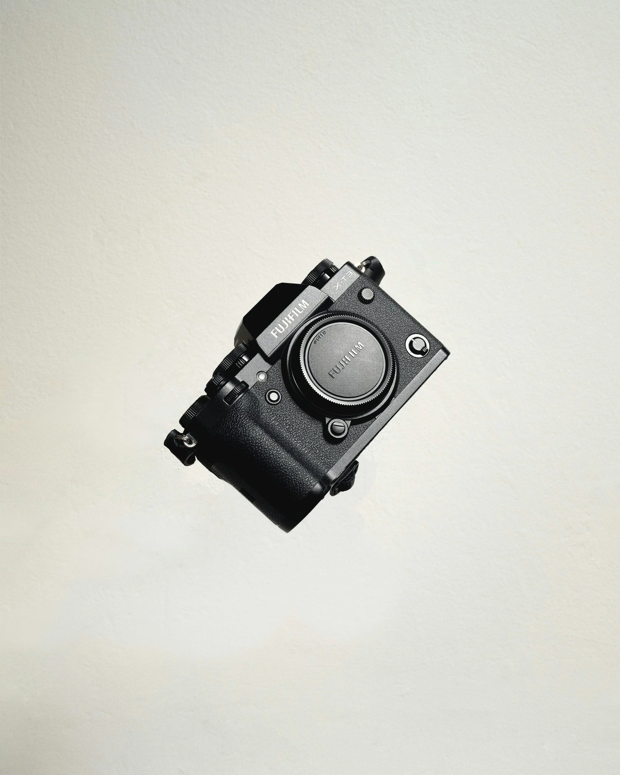 A black Fujifilm camera with a large lens, lying on a light gray surface.
