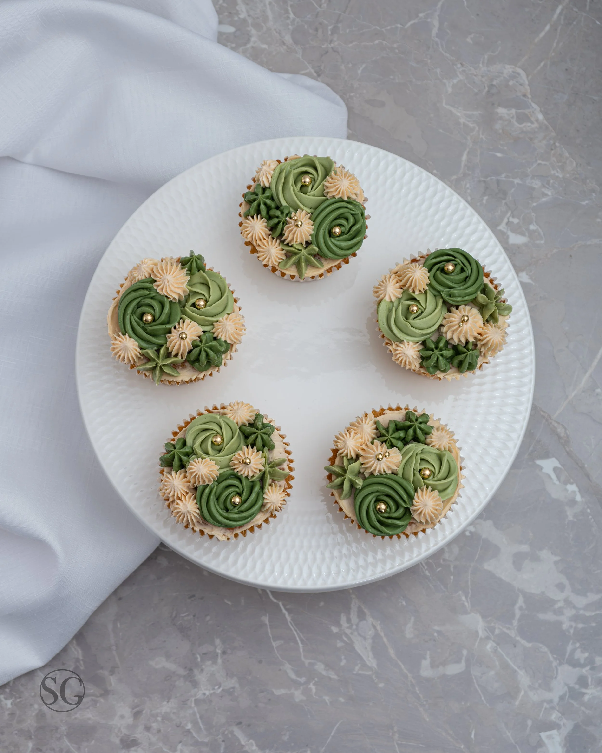 green frosted cupcakes on a white stand with a marble background