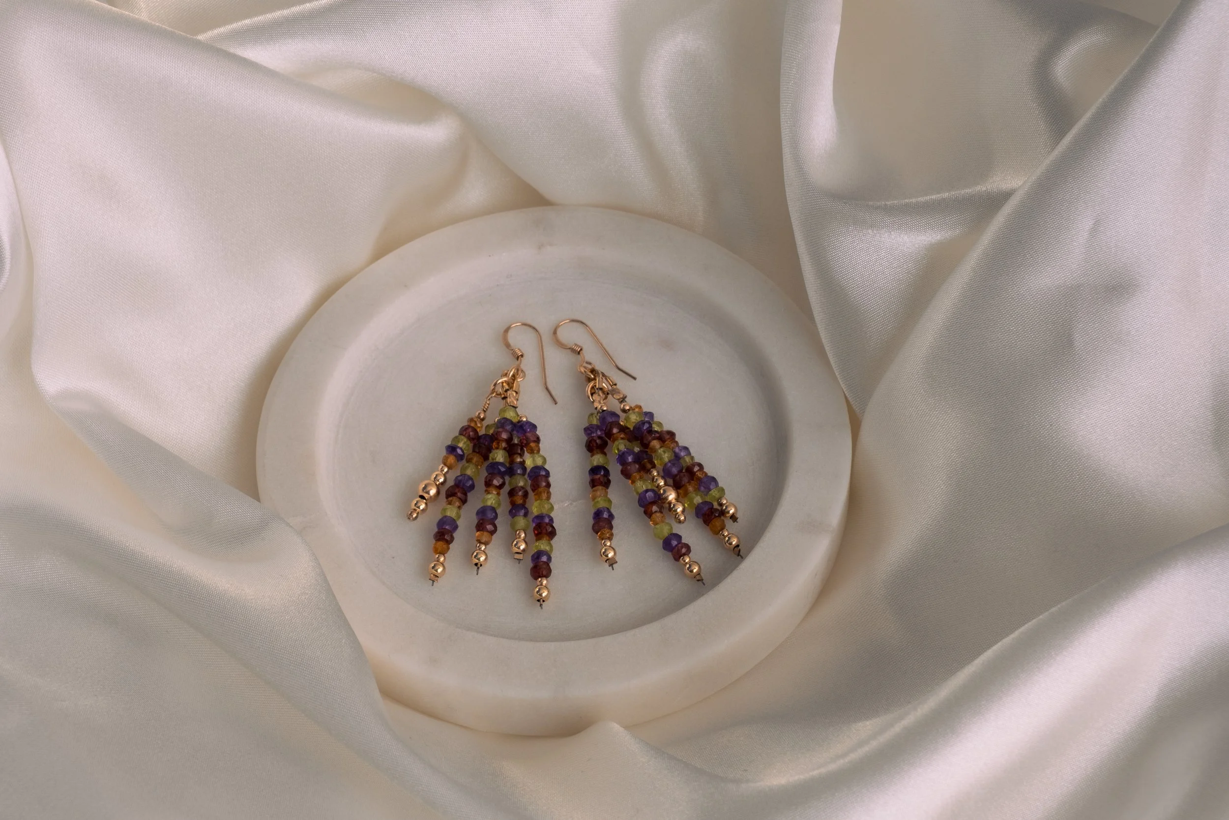 Colorful beaded necklace and earrings on a white satin fabric.