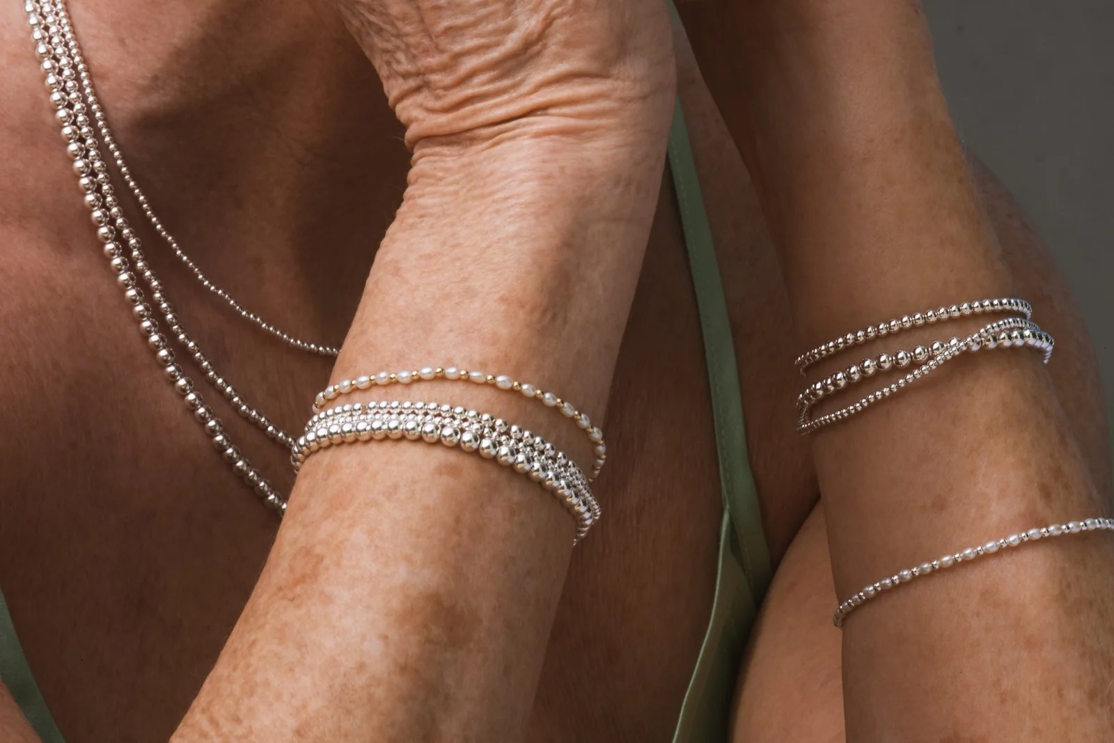 Close-up of a person's arm and shoulder adorned with multiple silver and pearl jewelry bracelets and necklaces.