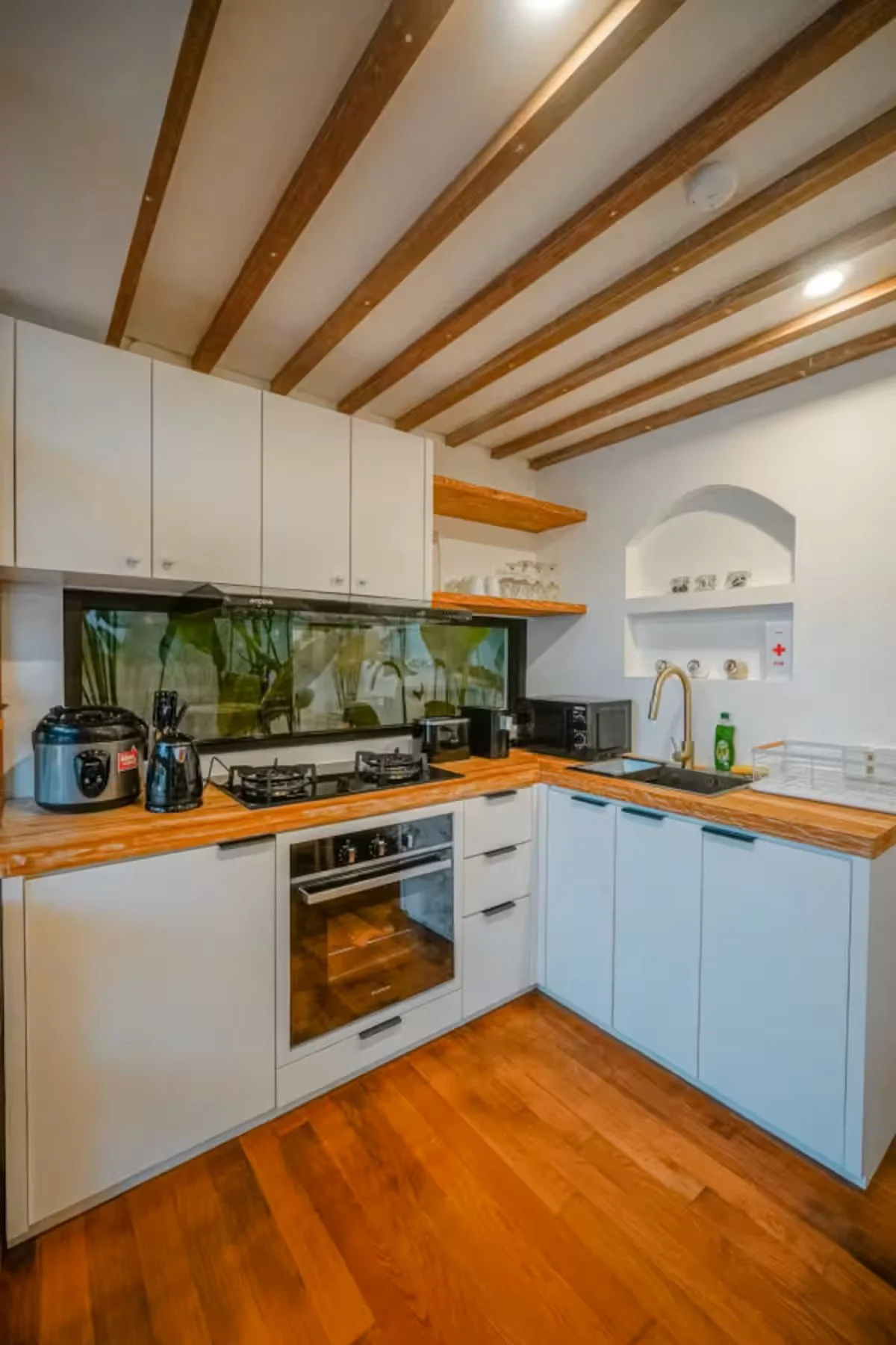 Kitchen with white cabinets, wooden countertops, and a wooden ceiling with exposed beams, featuring appliances like a microwave, oven, stovetop, and various small appliances.