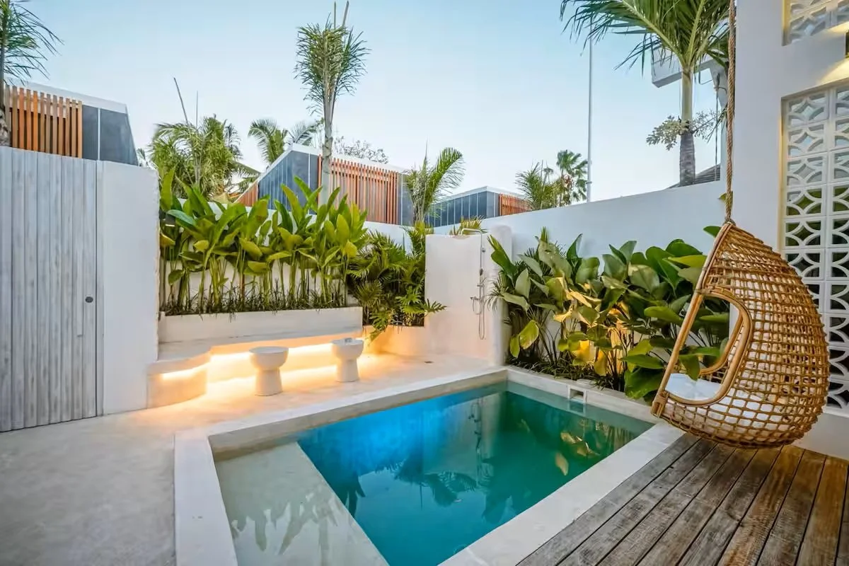 Private backyard with a small pool, tropical plants, and a woven hanging chair