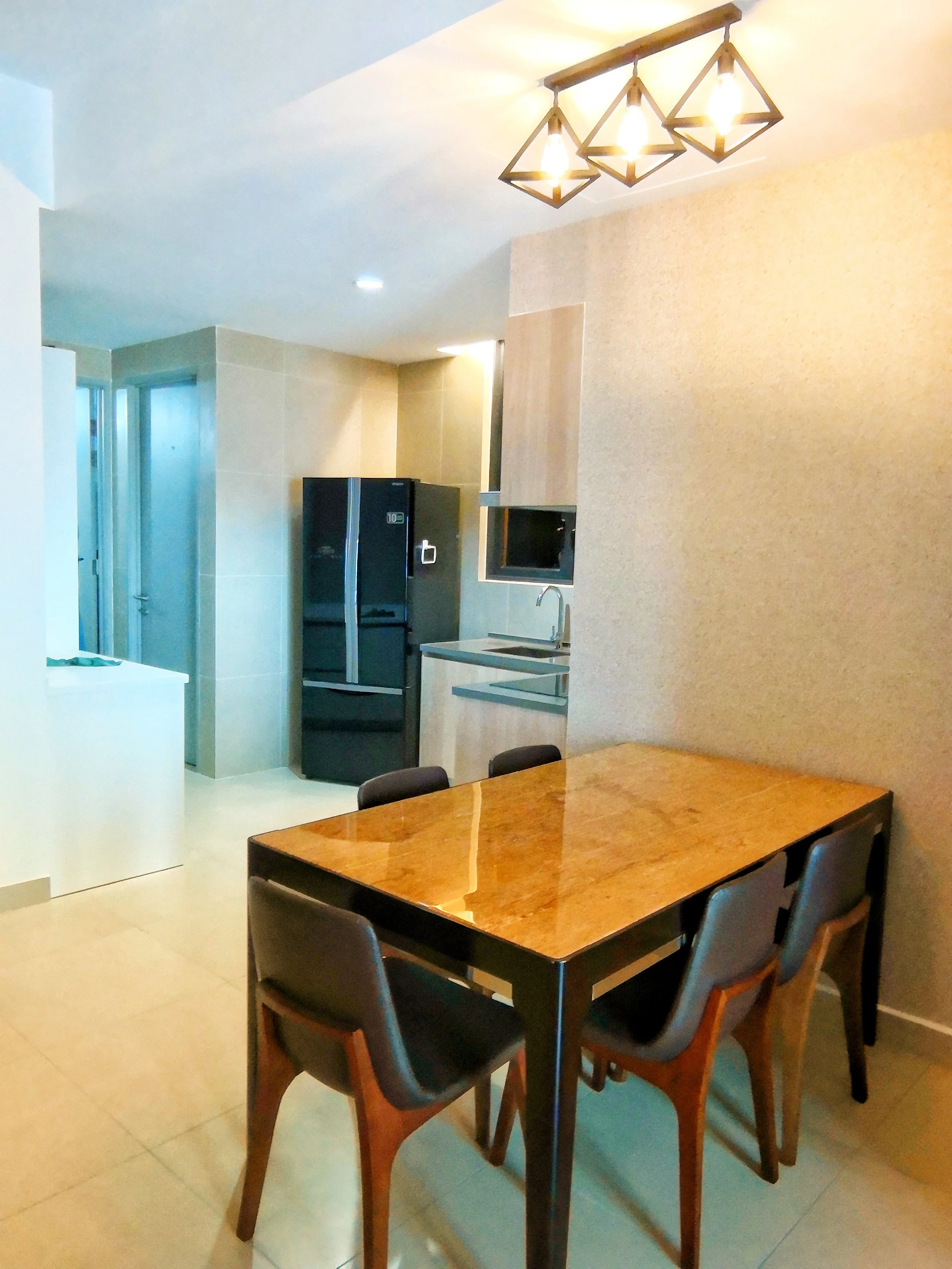 Kitchen and dining area with a wooden table and four black chairs, black refrigerator, sink, microwave, and abstract pendant light fixture.