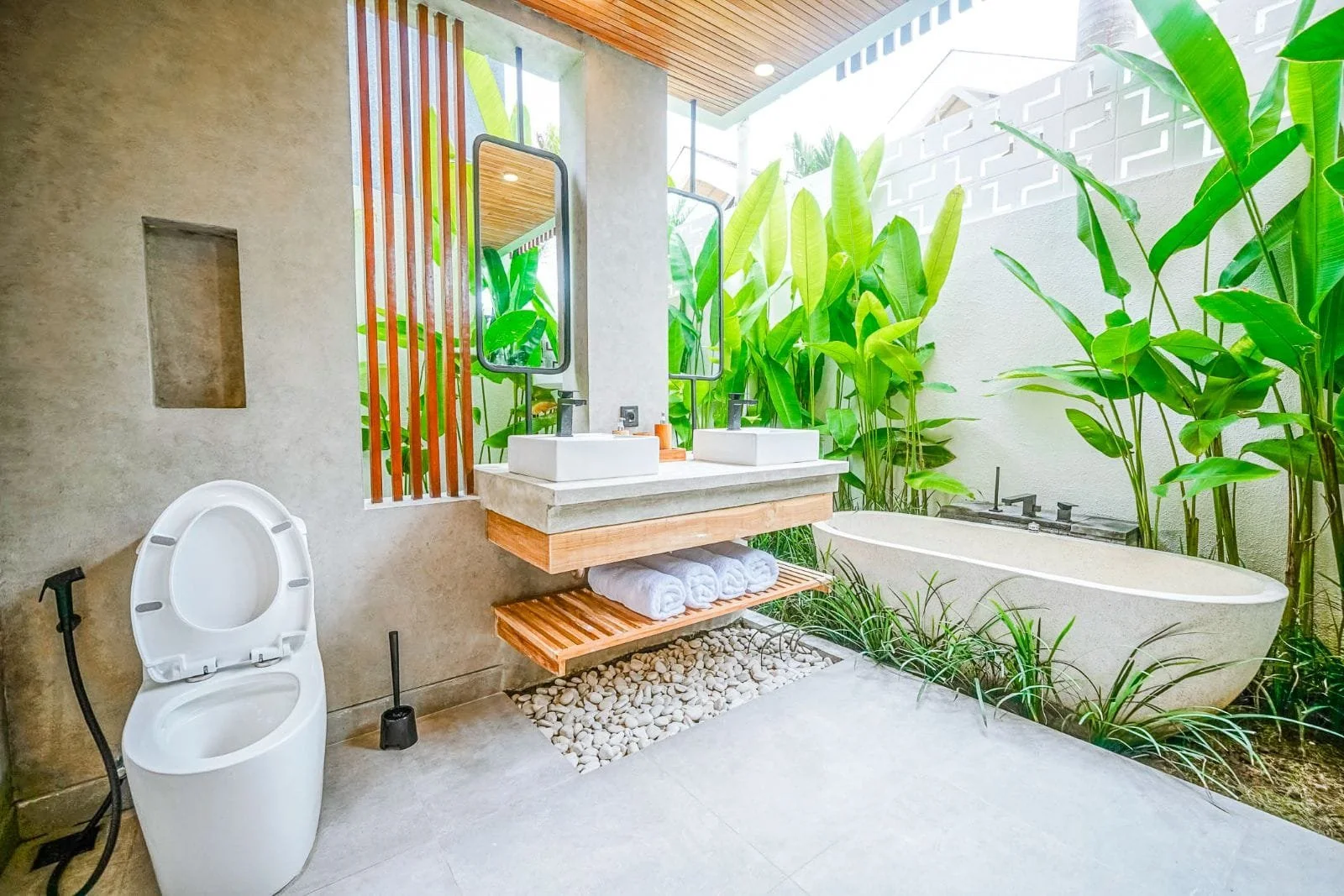 Bathroom with a modern bathtub, dual sinks with mirrors, and a tropical outdoor garden