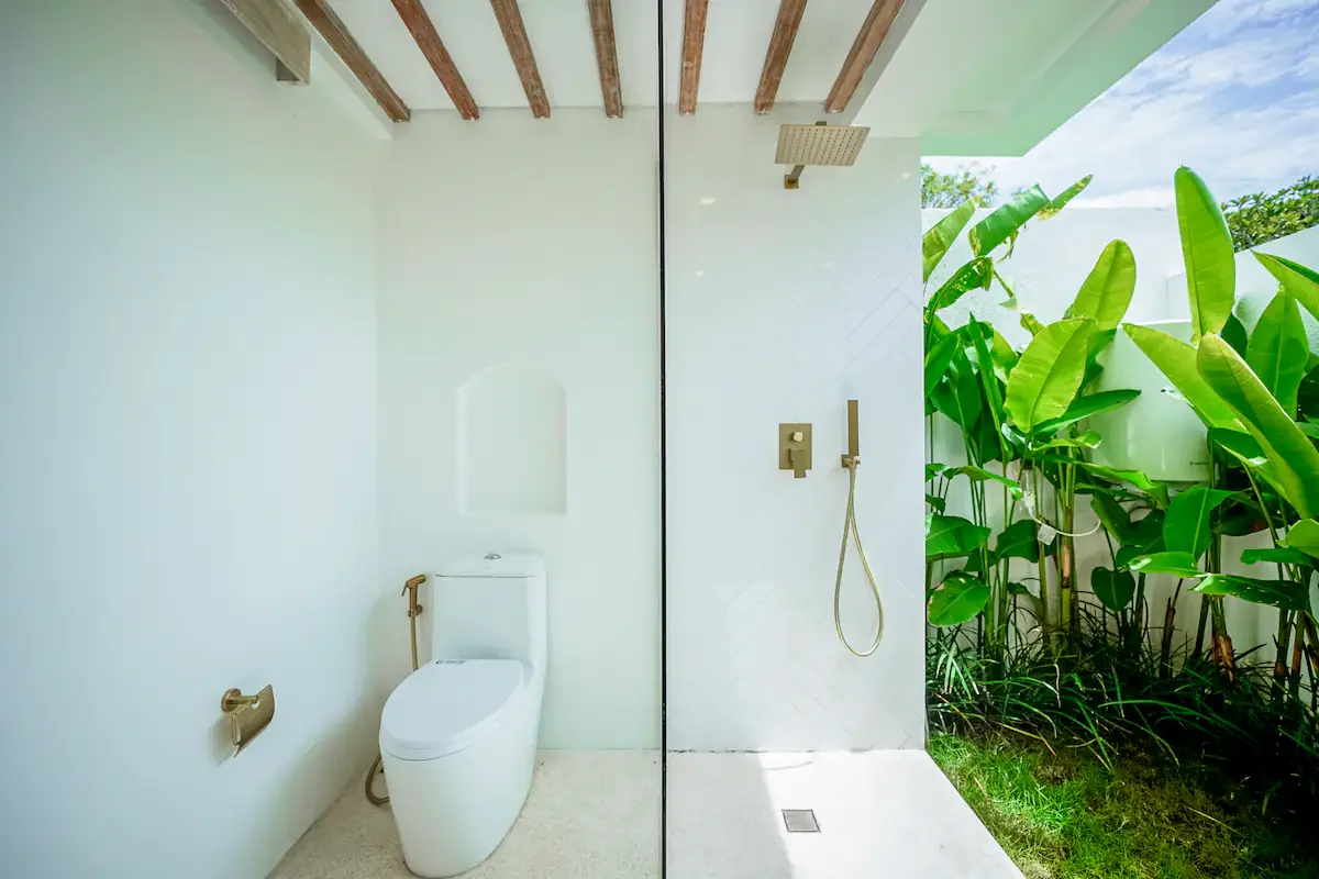 Bathroom with a toilet and an outdoor shower area with lush greenery.