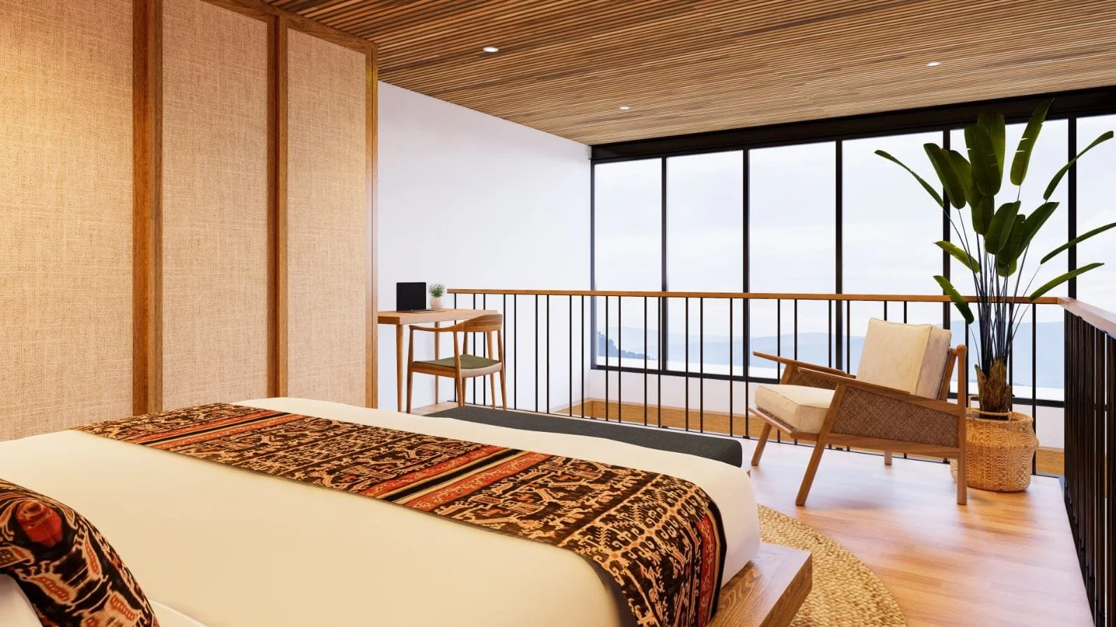 Modern hotel room with a bed, a small desk with a chair, a chair with a cushion, and a large potted plant near floor-to-ceiling windows showing a mountain view.