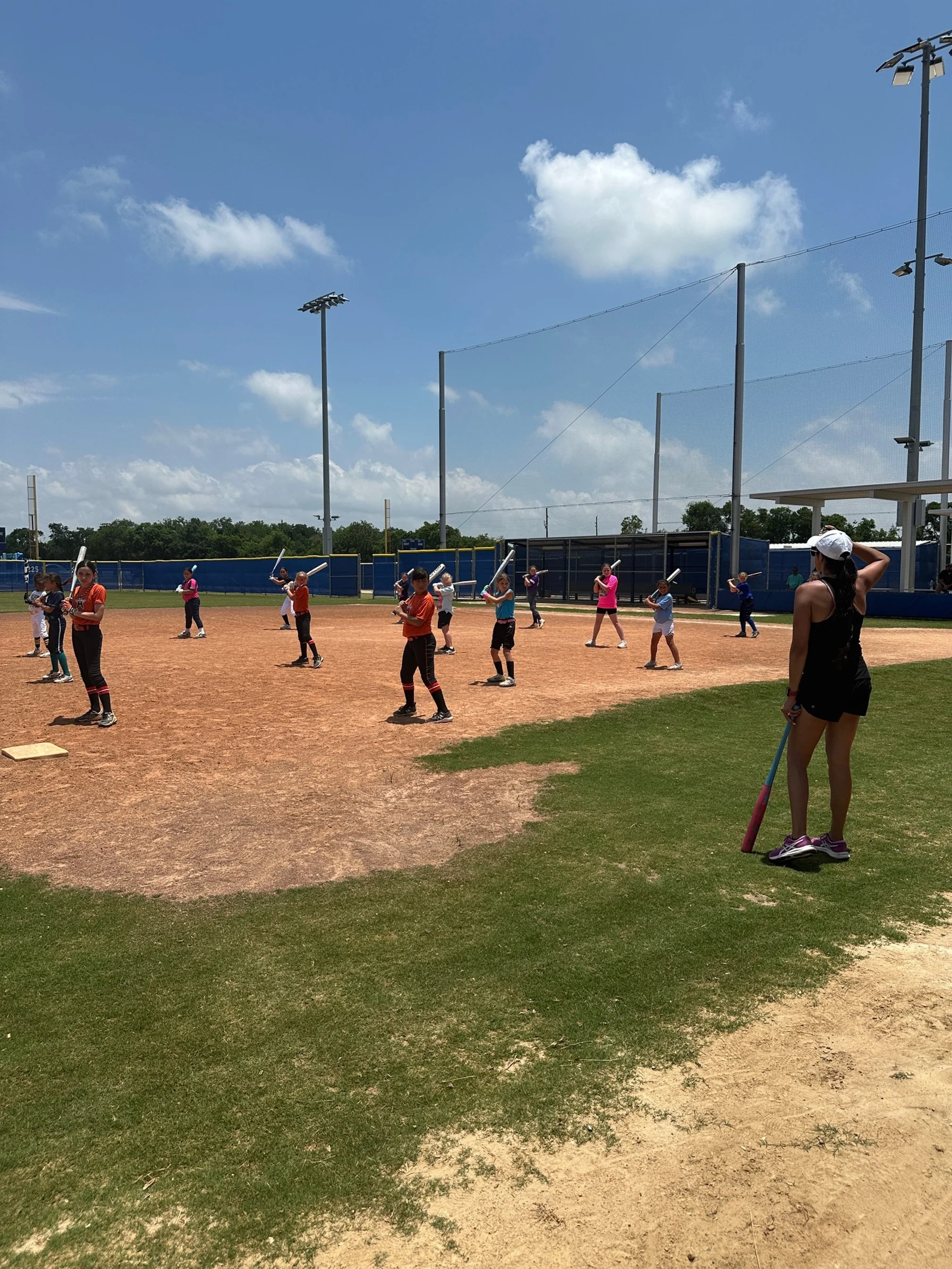 A softball clinic on a sunny day at a softball field with players holding bats, working with The Softball Doctor, Jessica Bowden.