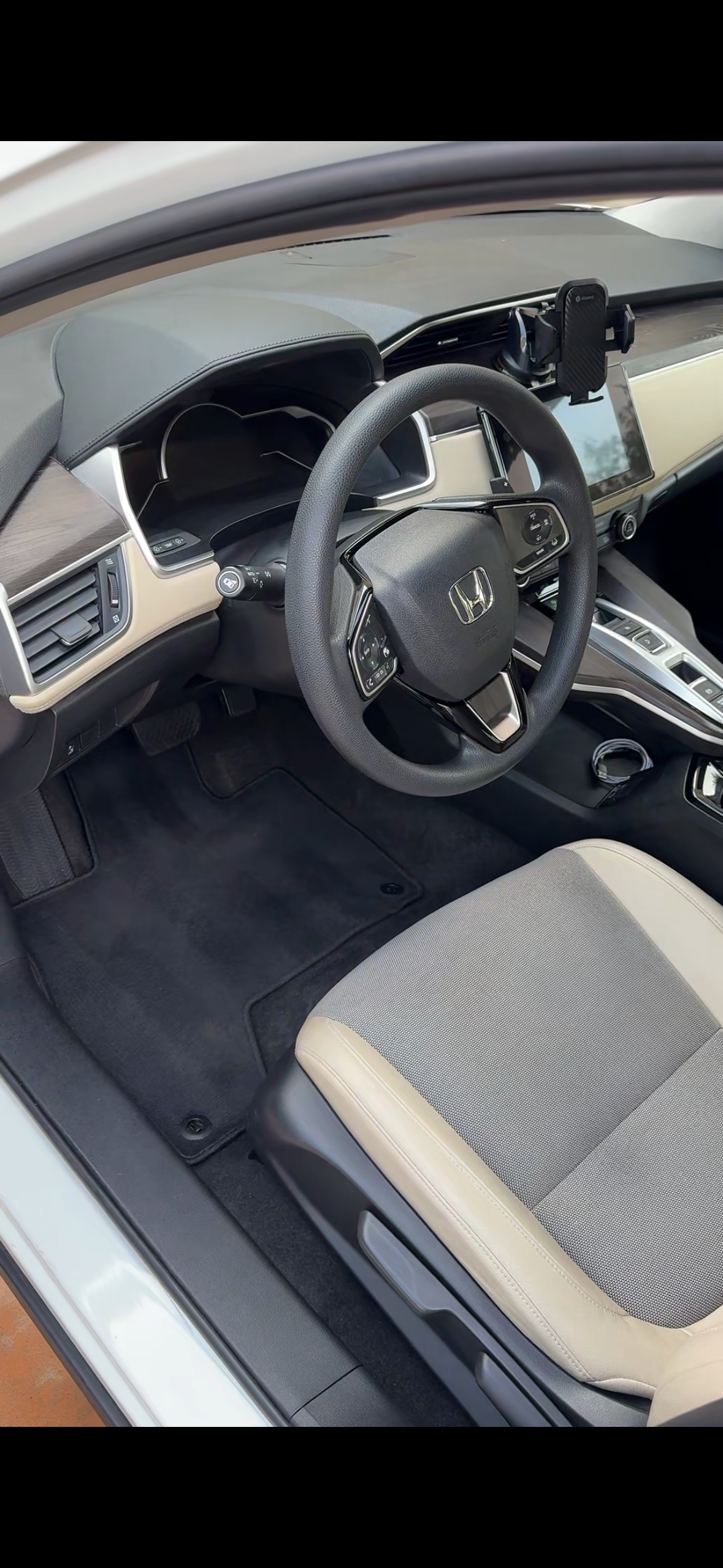 Interior of a Honda car showing the steering wheel, dashboard, and front passenger seat with smartphone holder attached to the dashboard.