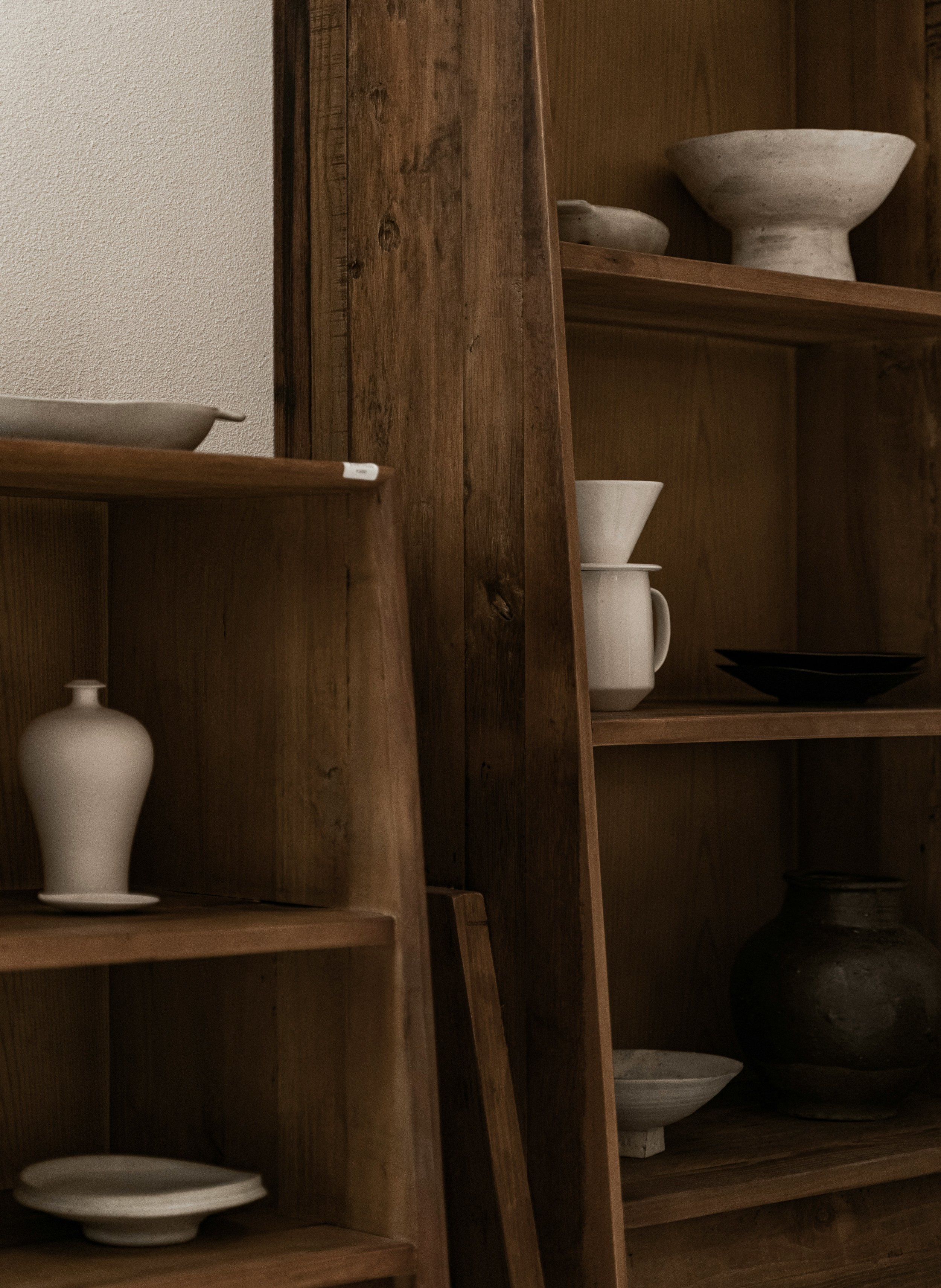 Wooden shelves with various pottery items including bowls, plates, and a pitcher in a dimly lit room.