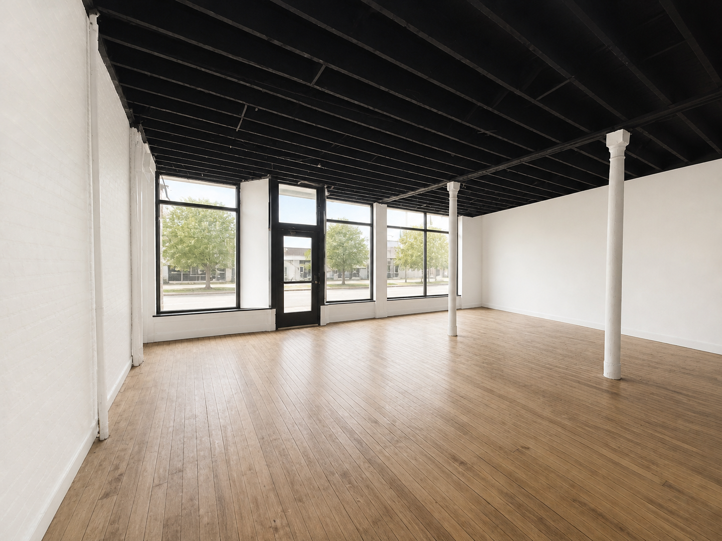 Empty commercial space with wood flooring, large windows, white brick walls, black ceiling, and white support columns.