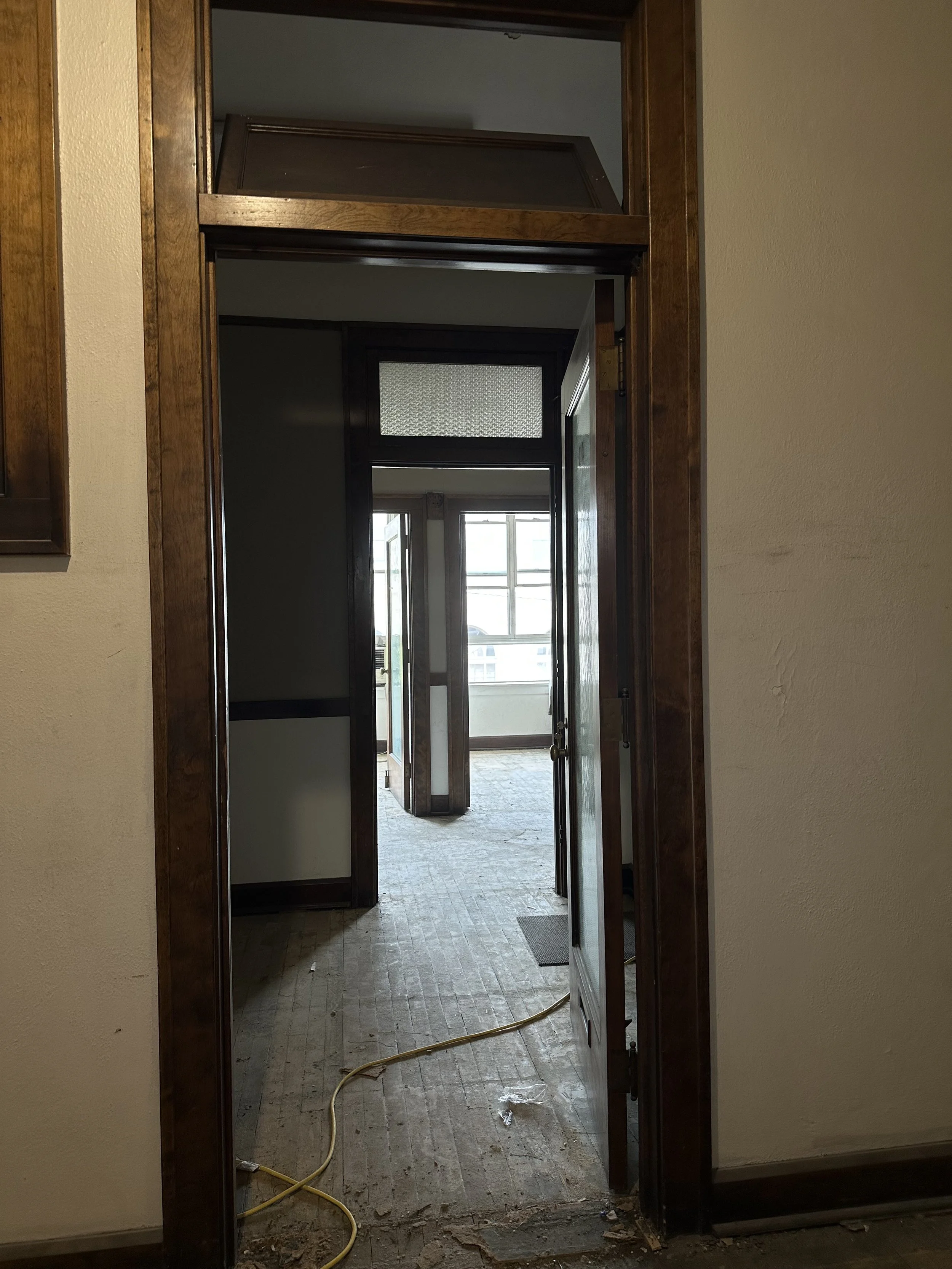 Interior view of a doorway with a cut-out in the door frame, showing a hallway with large windows and a door at the end, suggesting a renovation or construction project.