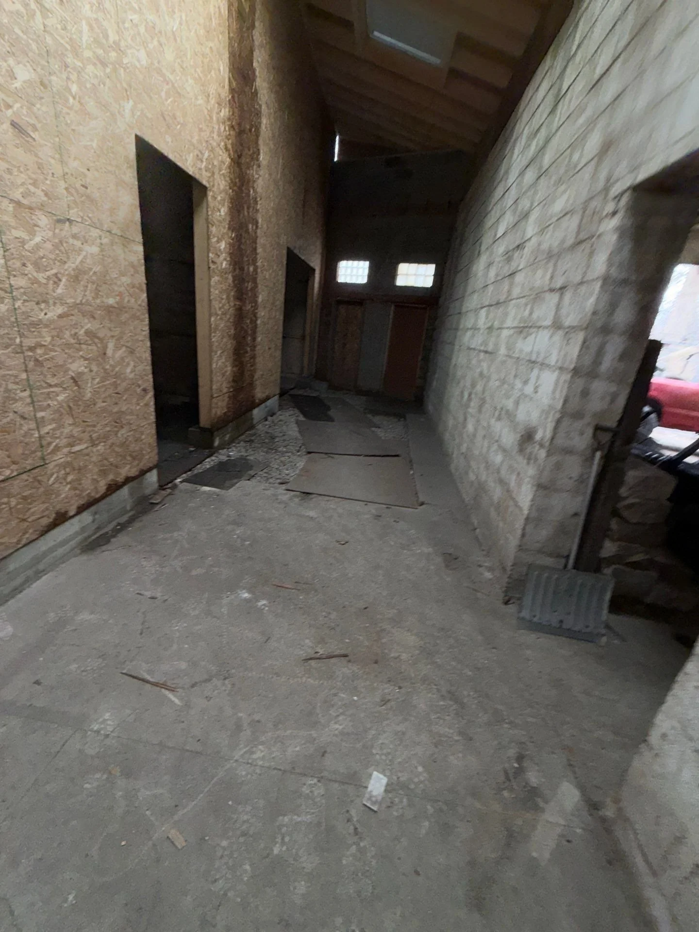 Unfinished interior space with concrete floor, partially boarded wood walls, and small windows on the back wall.
