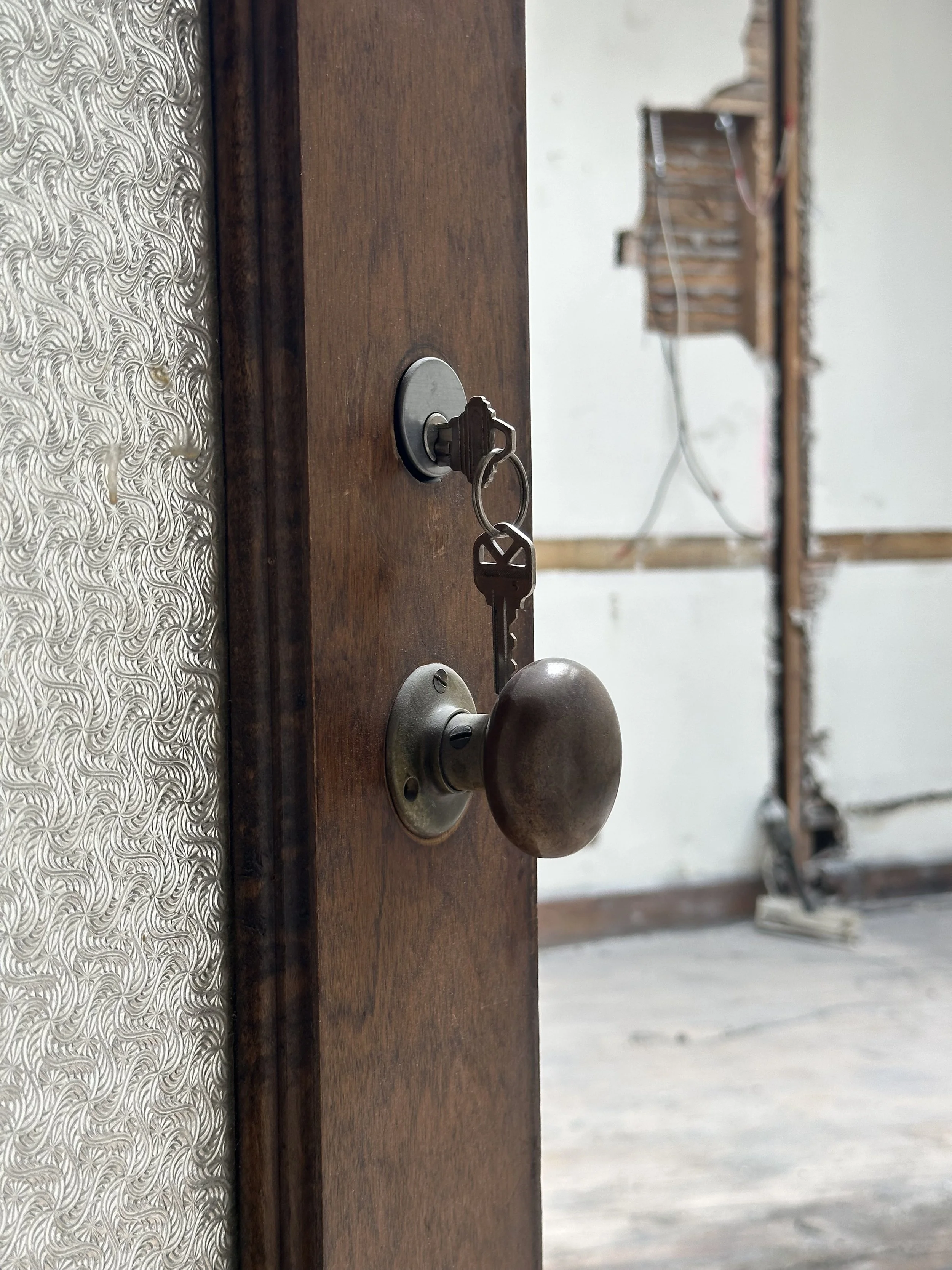 Close-up of a wooden door with a lock and a brass doorknob, partially open in an unfinished room.