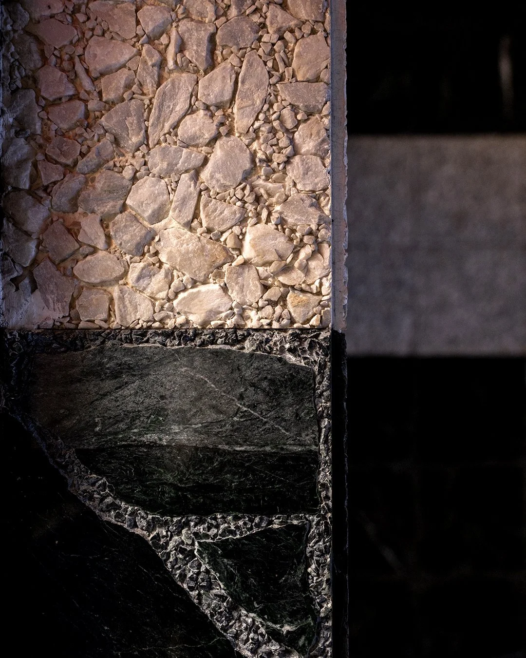 Close-up of a cross-section of a layered rock with crushed stones at the top, dark dark greenish layer in the middle, and a black layer at the bottom.